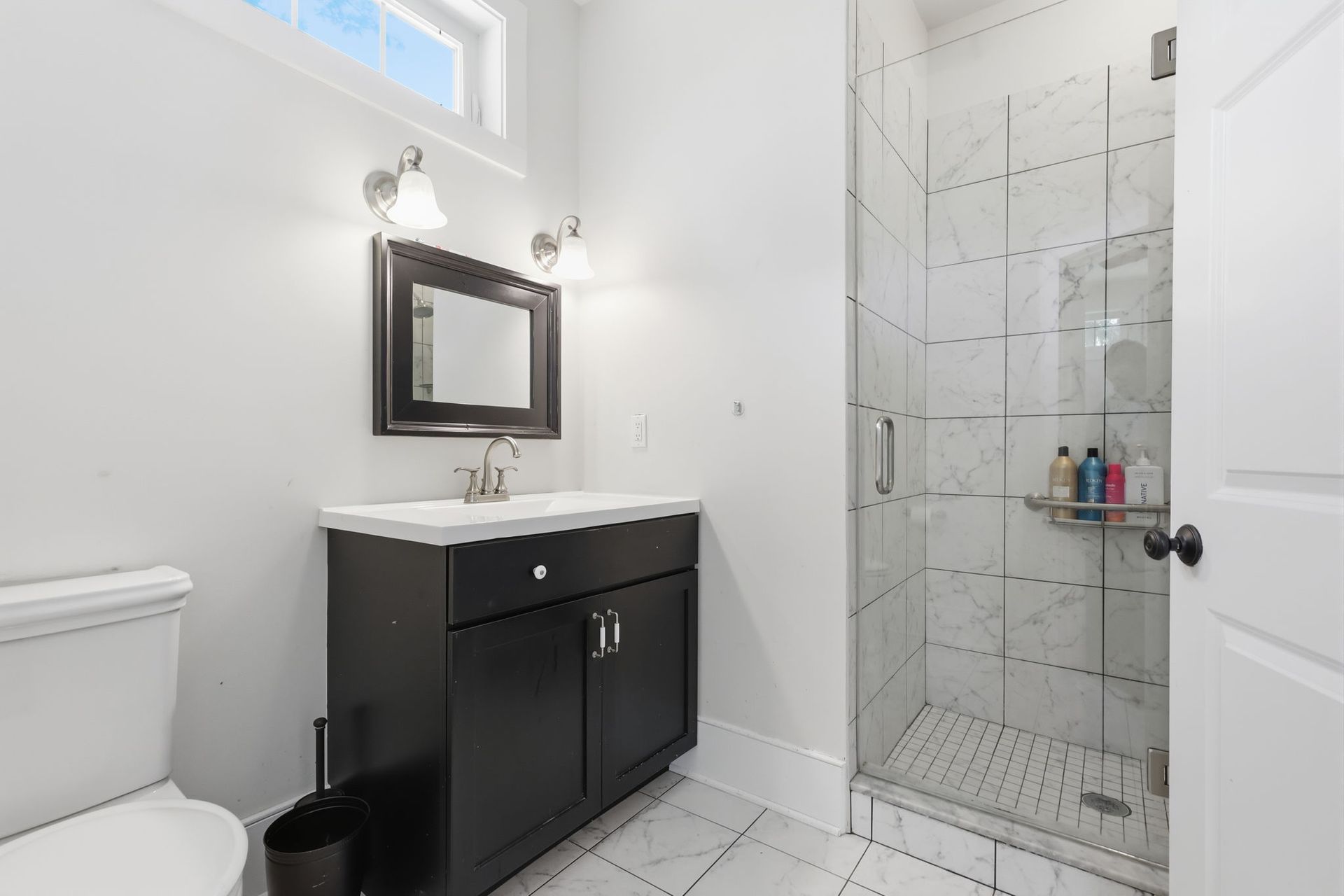 Modern white bathroom with black vanity, mirror, toilet, and glass shower