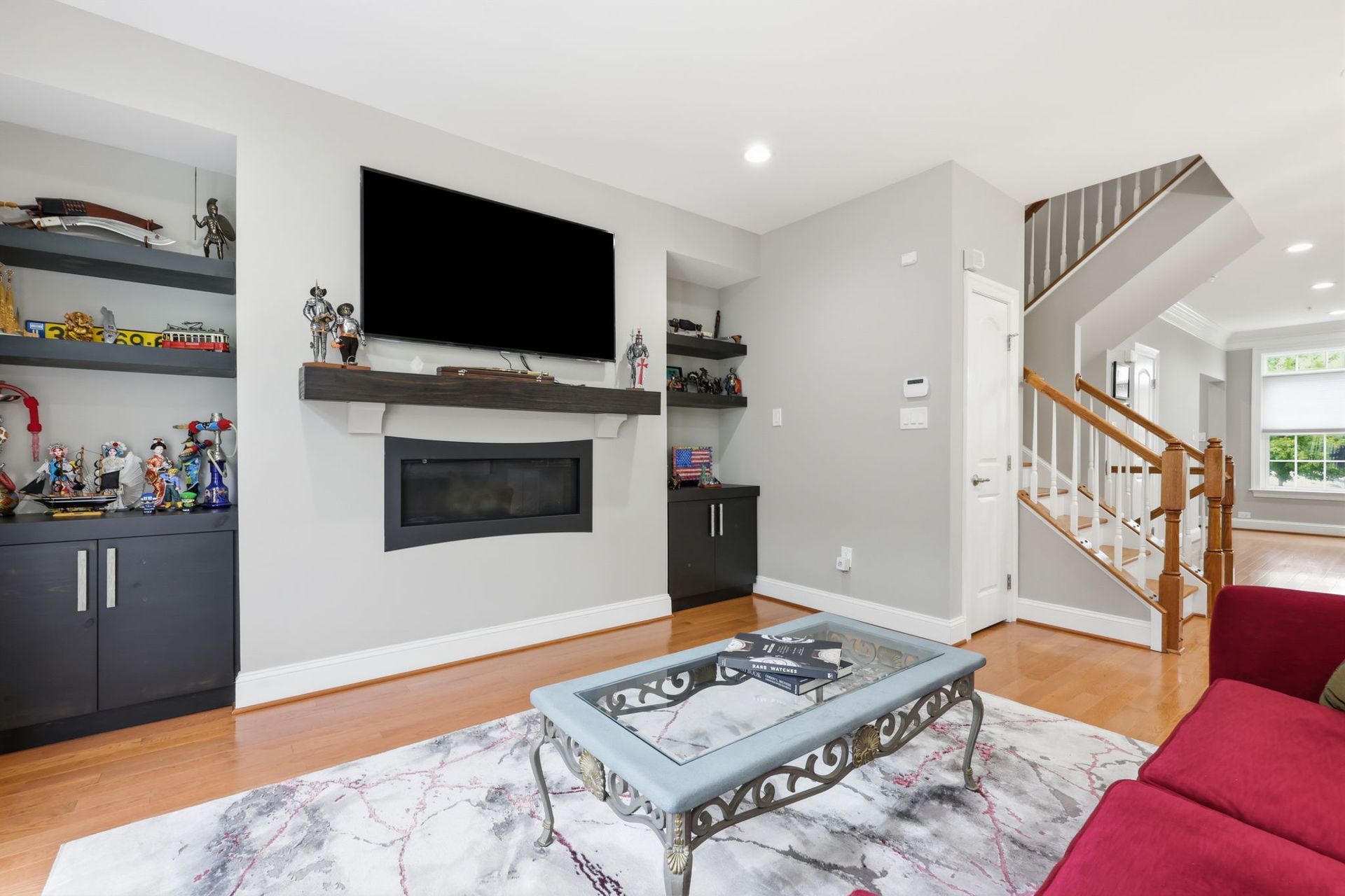 Modern living room with fireplace, TV, red sofa, glass coffee table, and staircase.