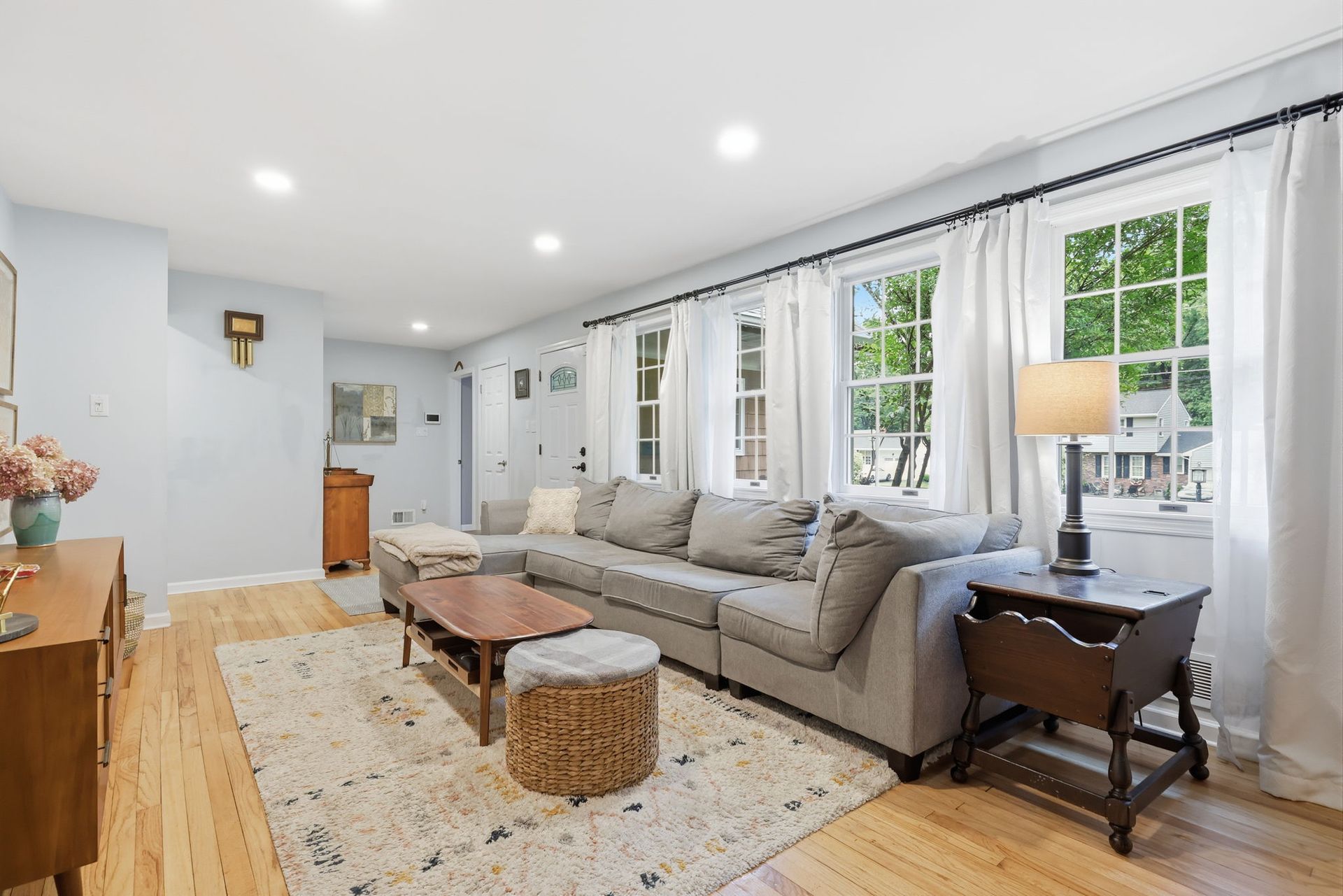 Bright living room with gray sofa, white walls, wood table, and large windows along one side