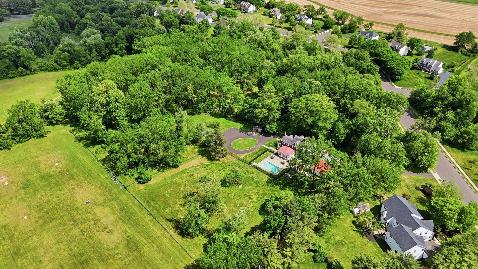 Aerial view of a rural property with dense green trees, a small house, and surrounding fields