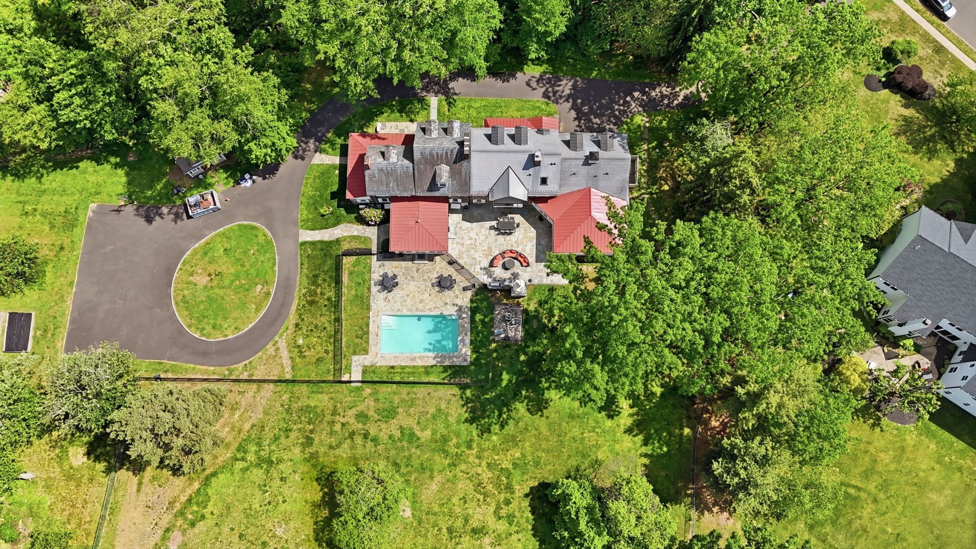 Aerial view of a large house with a swimming pool, circular driveway, and dense green trees around it