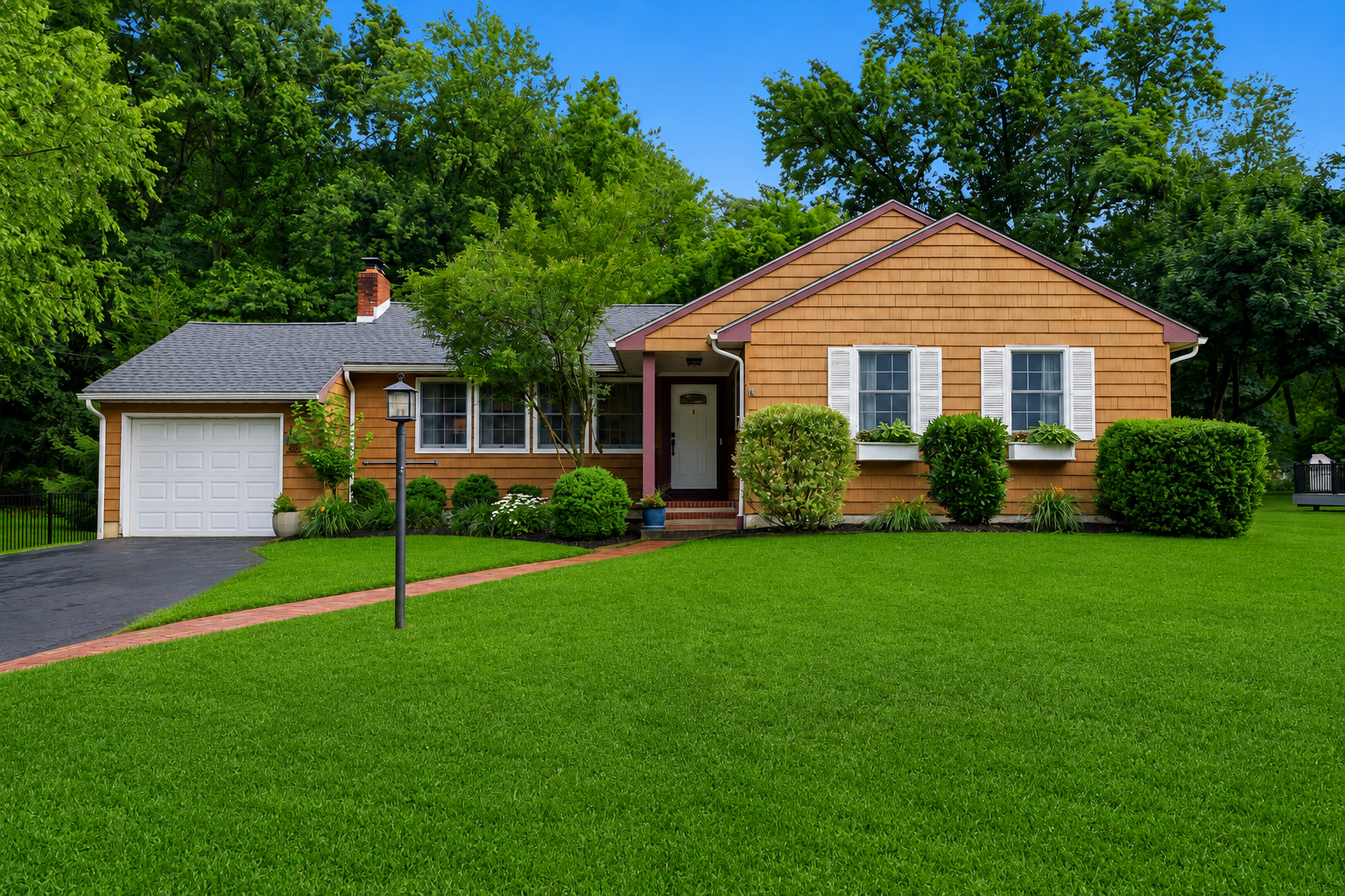Suburban brick house with a two-car garage, green lawn, and trees in the background