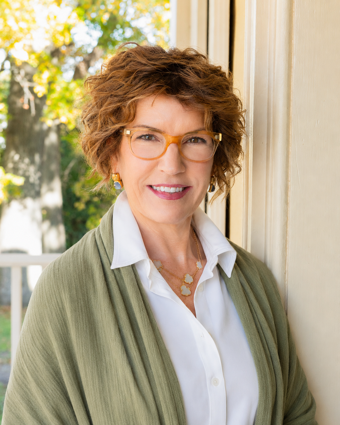 Heather Jackman-Portrait of a smiling woman in glasses and a green shawl standing by a sunlit doorway