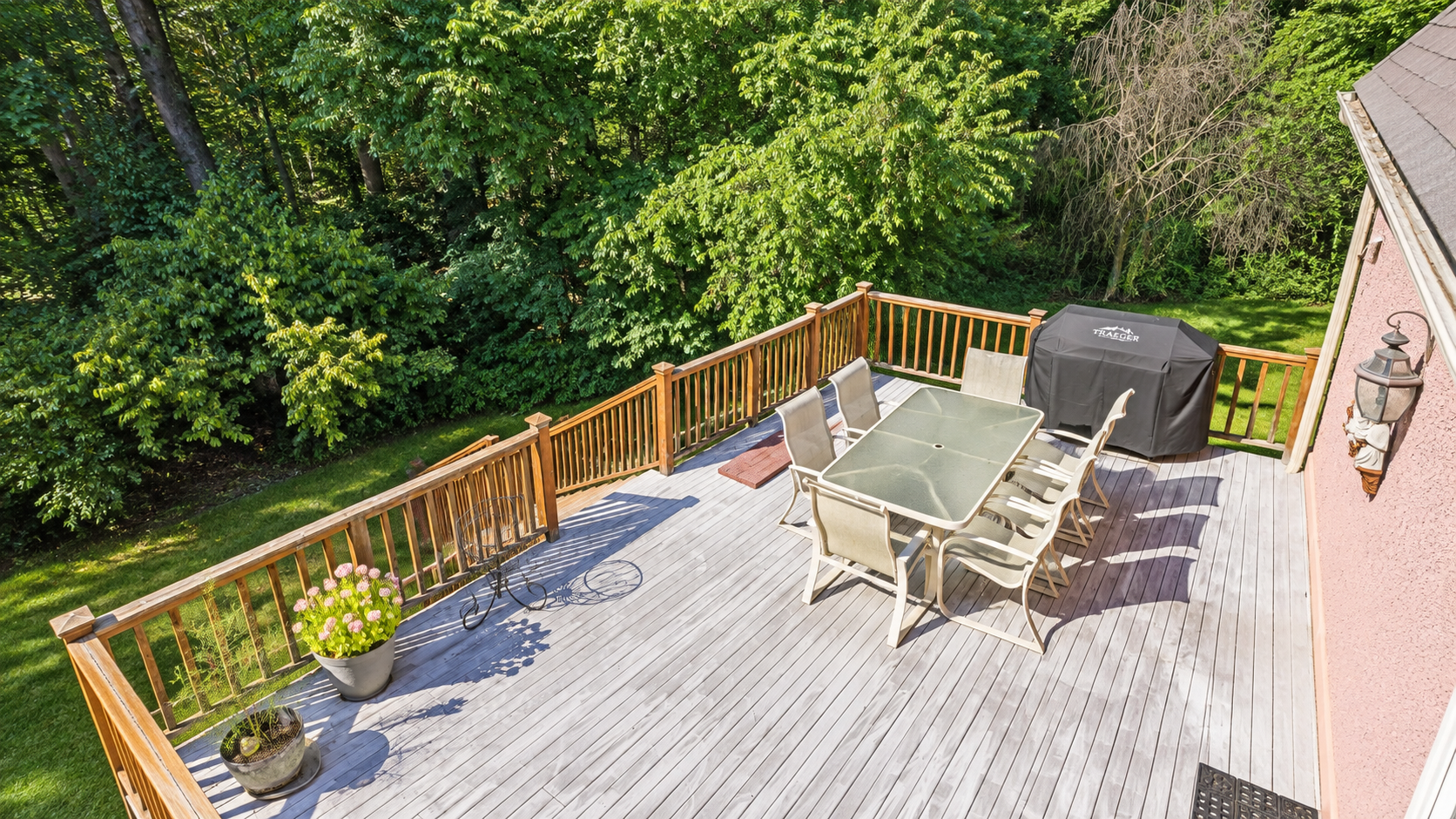 Patio deck with table, chairs, grill, and potted plants overlooking green trees
