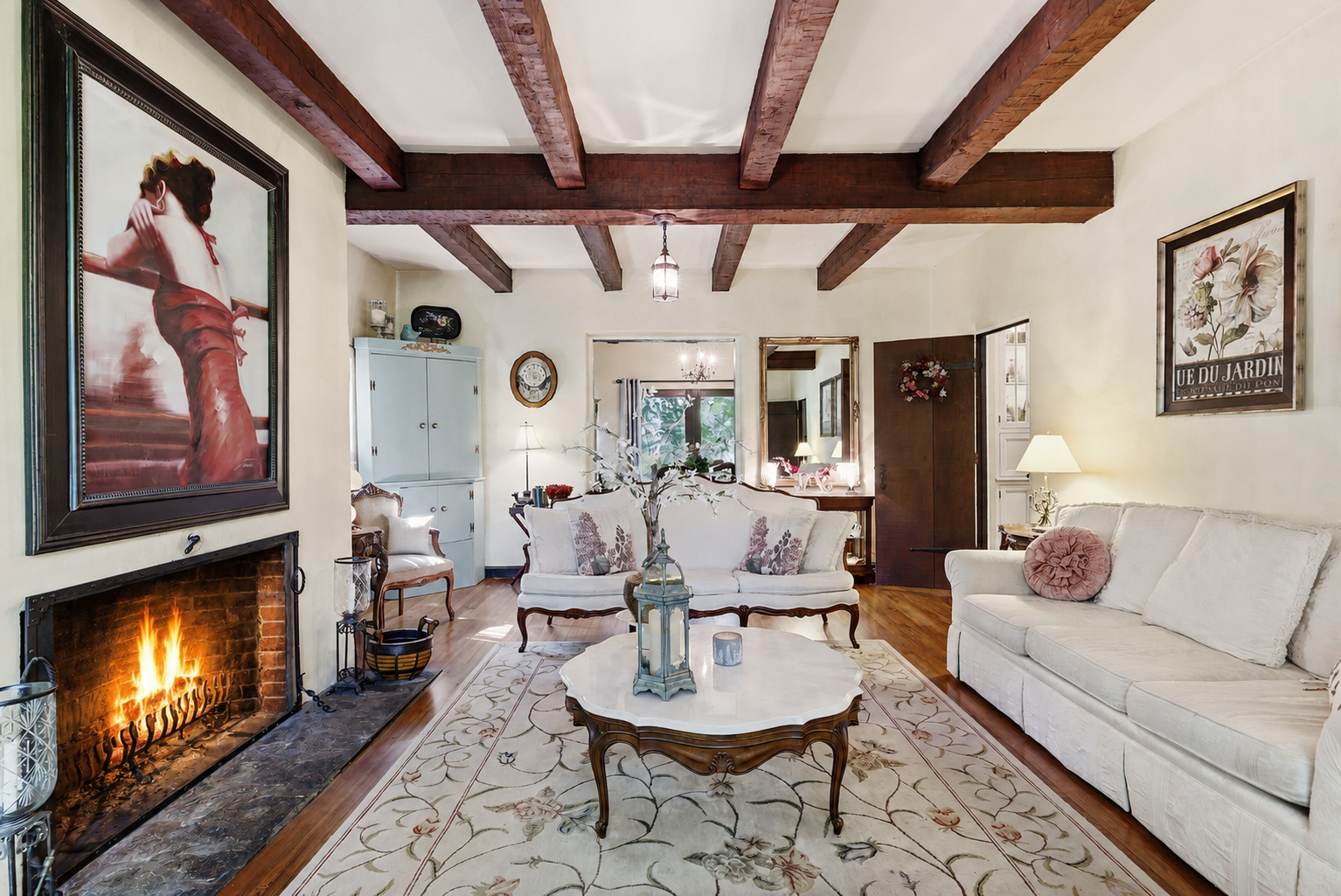 Cozy living room with a lit fireplace, white sofa, coffee table, and exposed wooden ceiling beams.