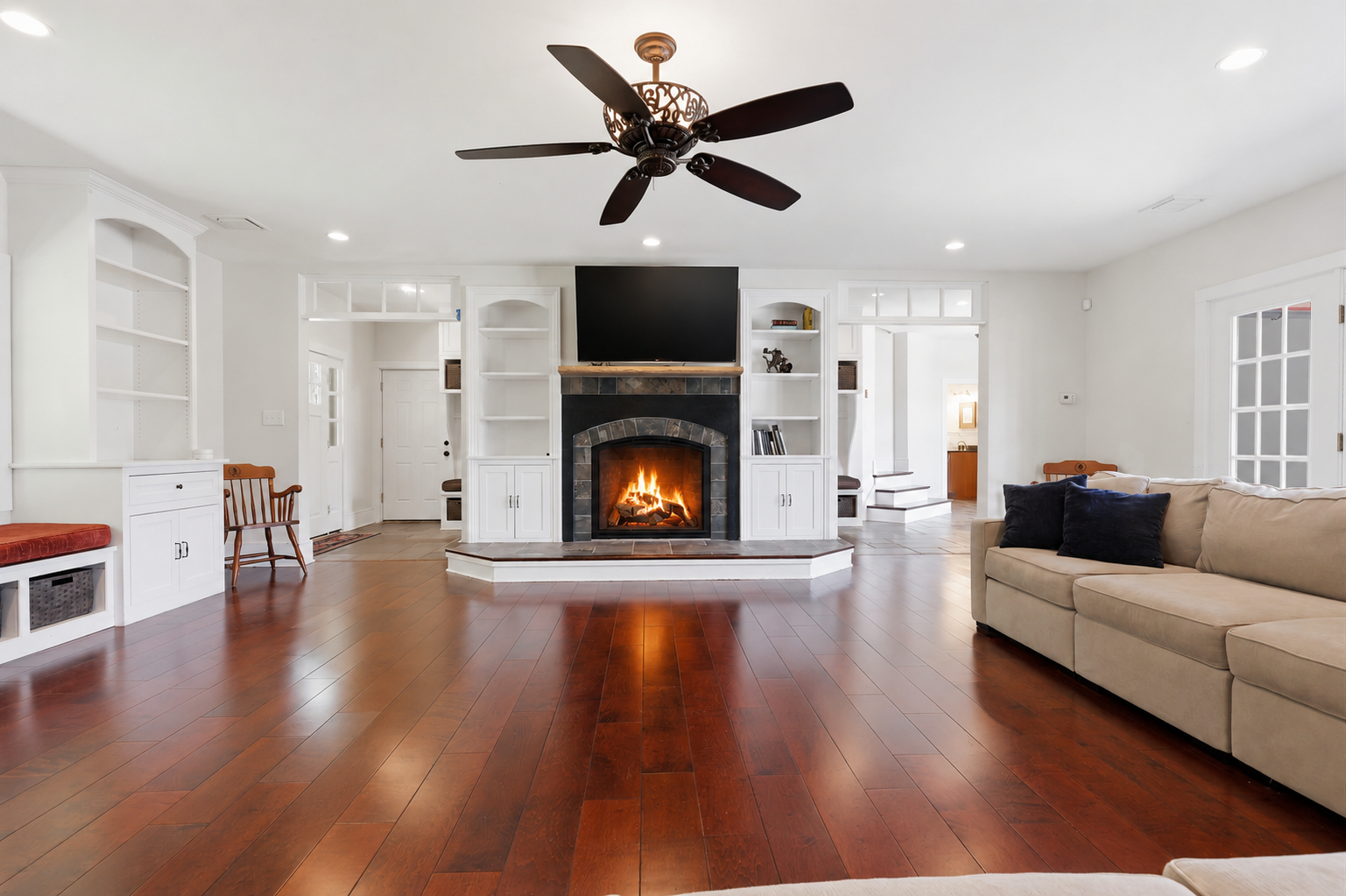 Bright living room with hardwood floors, fireplace, beige sofa, and ceiling fan under recessed lights