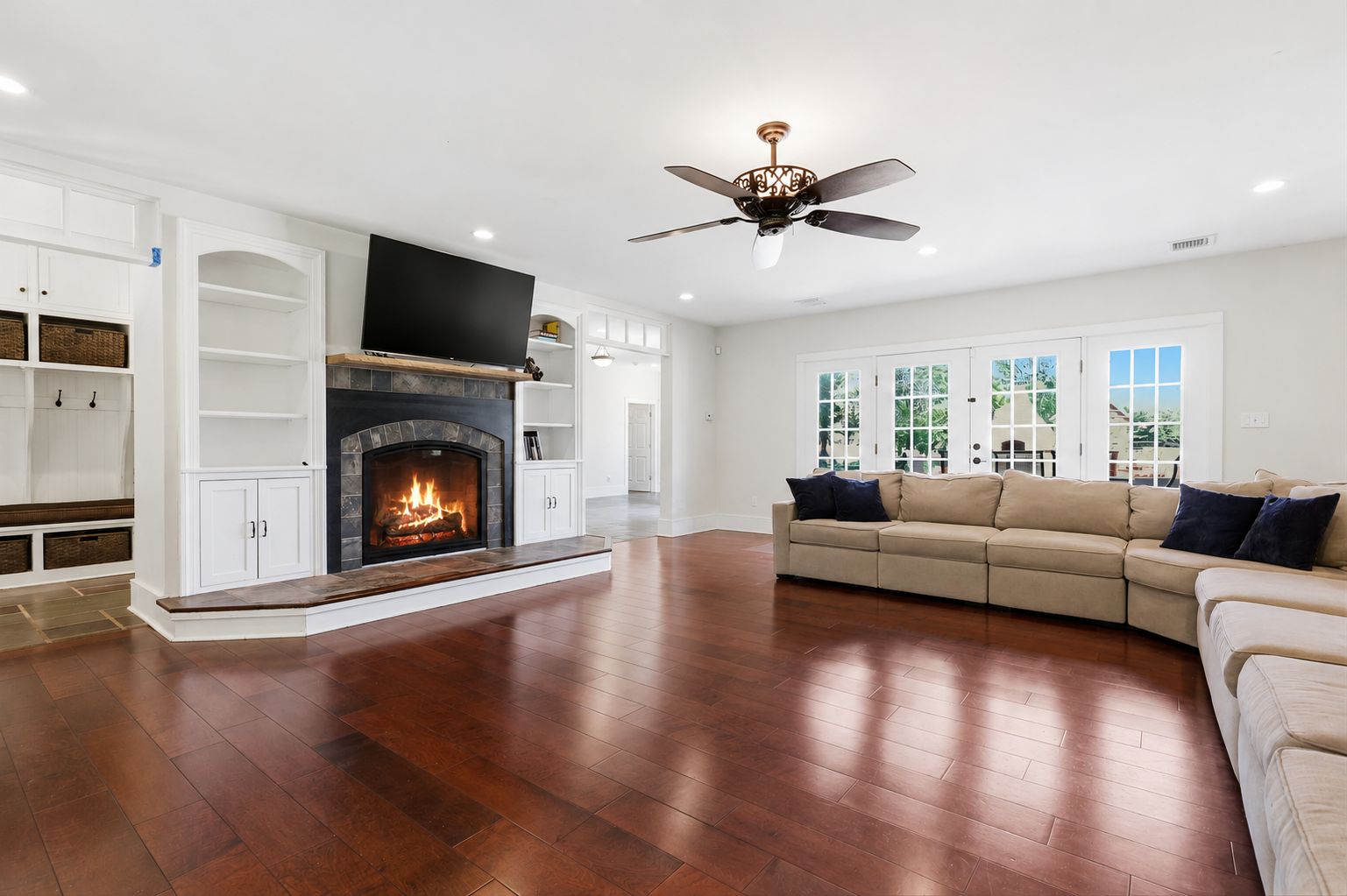 Bright living room with fireplace, hardwood floors, beige sectional, ceiling fan, and large windows with daylight