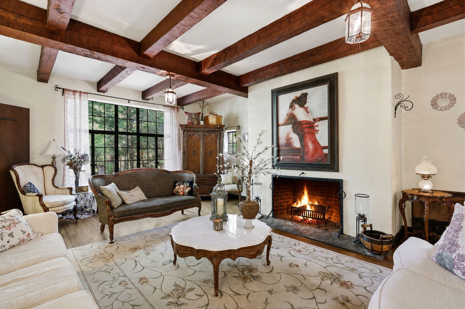 Cozy living room with exposed beams, fireplace, floral sofa, and large window.