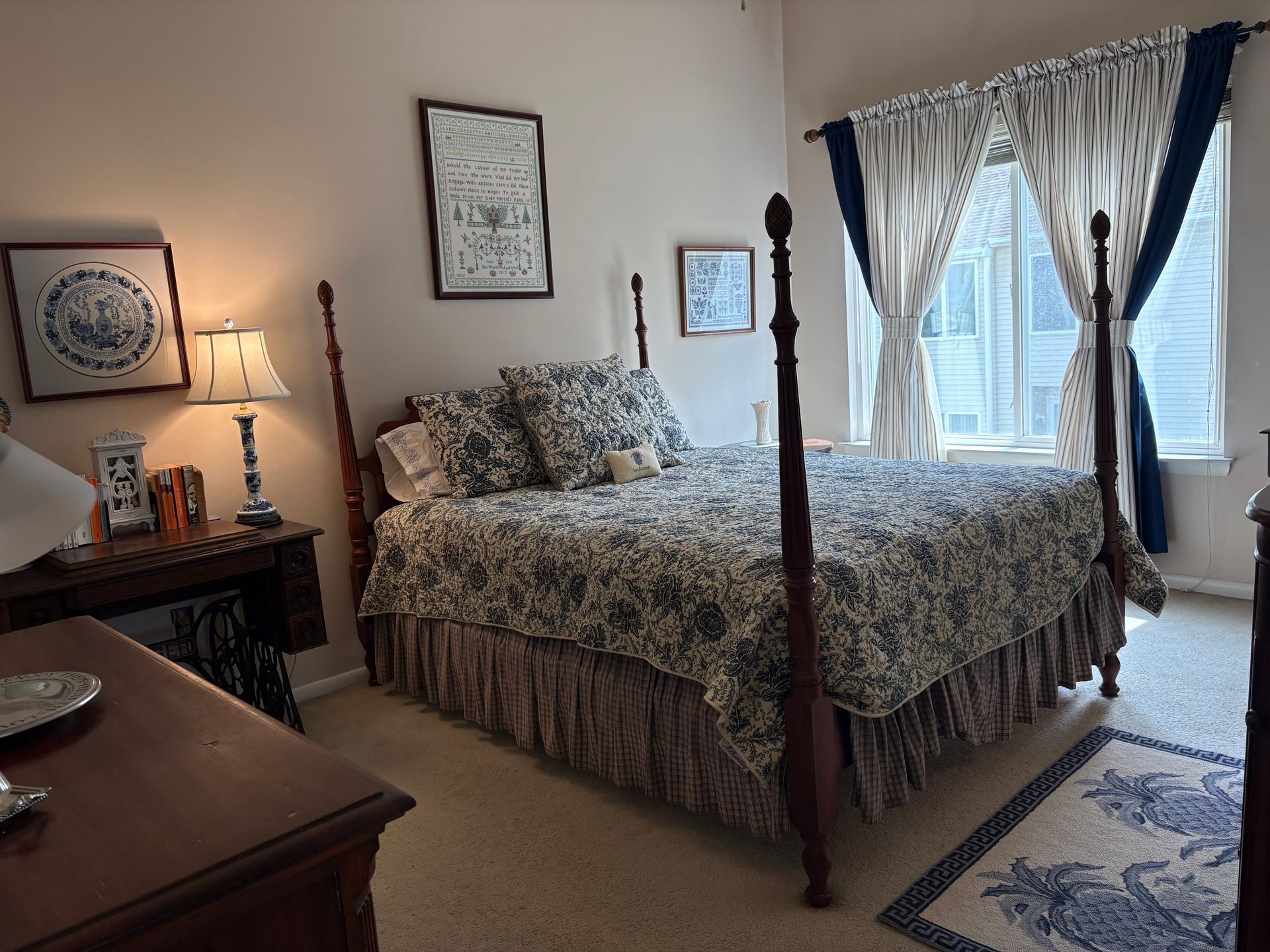 Cozy bedroom with a four-poster bed, floral bedding, bedside lamp, and large window with curtains