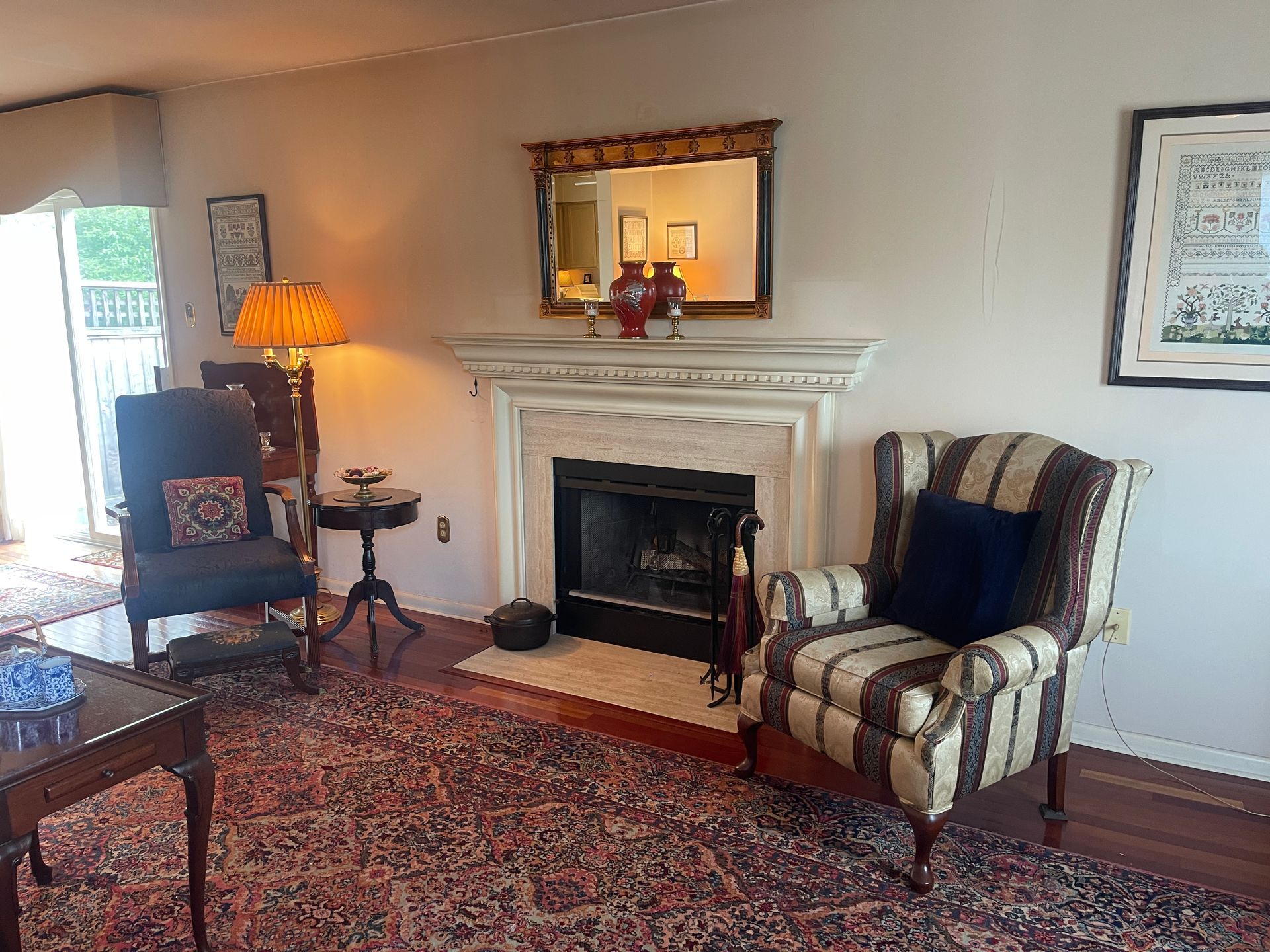 Cozy living room with fireplace, patterned rug, striped armchair, lamp, and framed art on cream walls