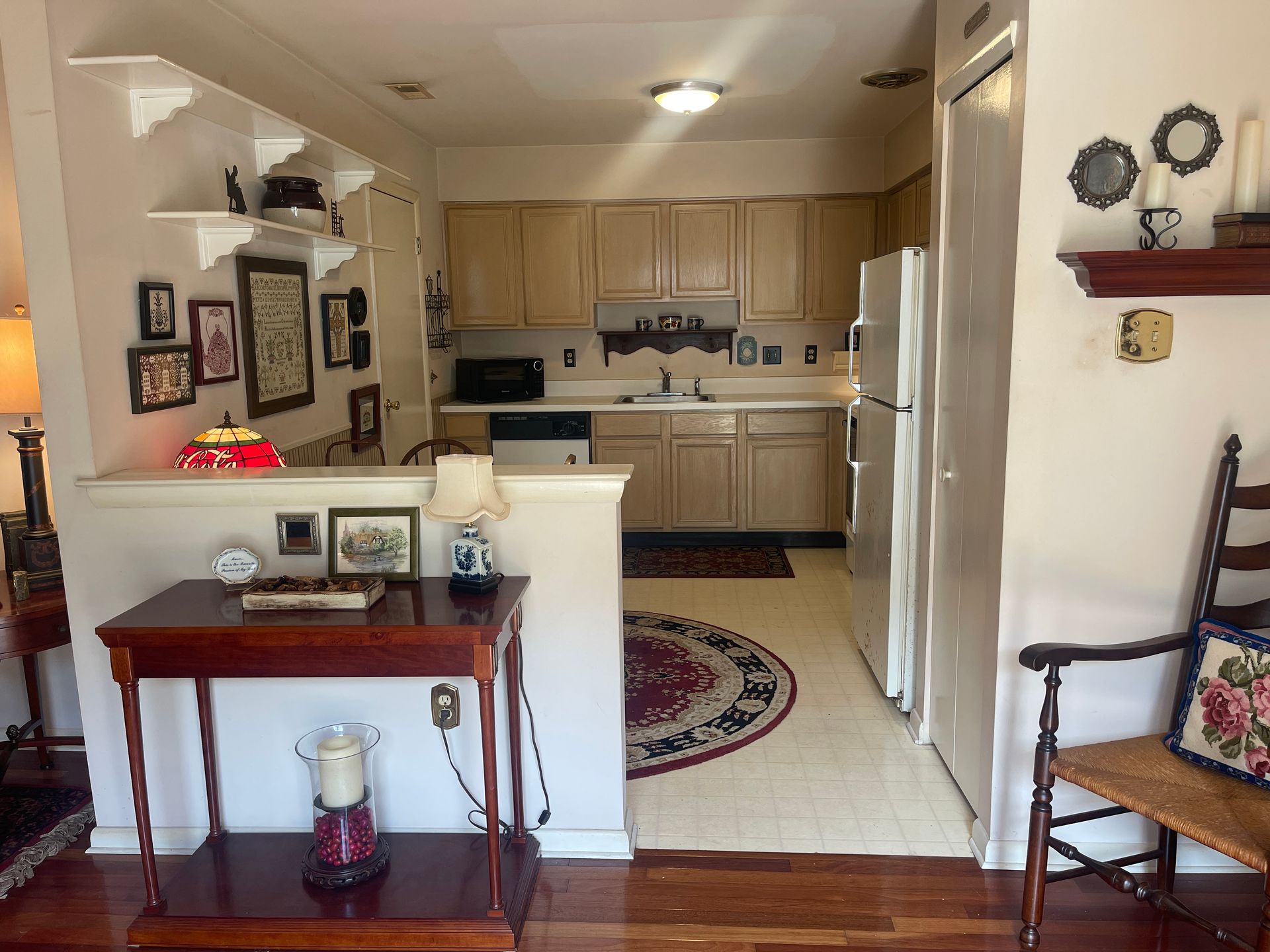 Cozy living room opening to a kitchen, with a small table, wall decor, and beige cabinets.