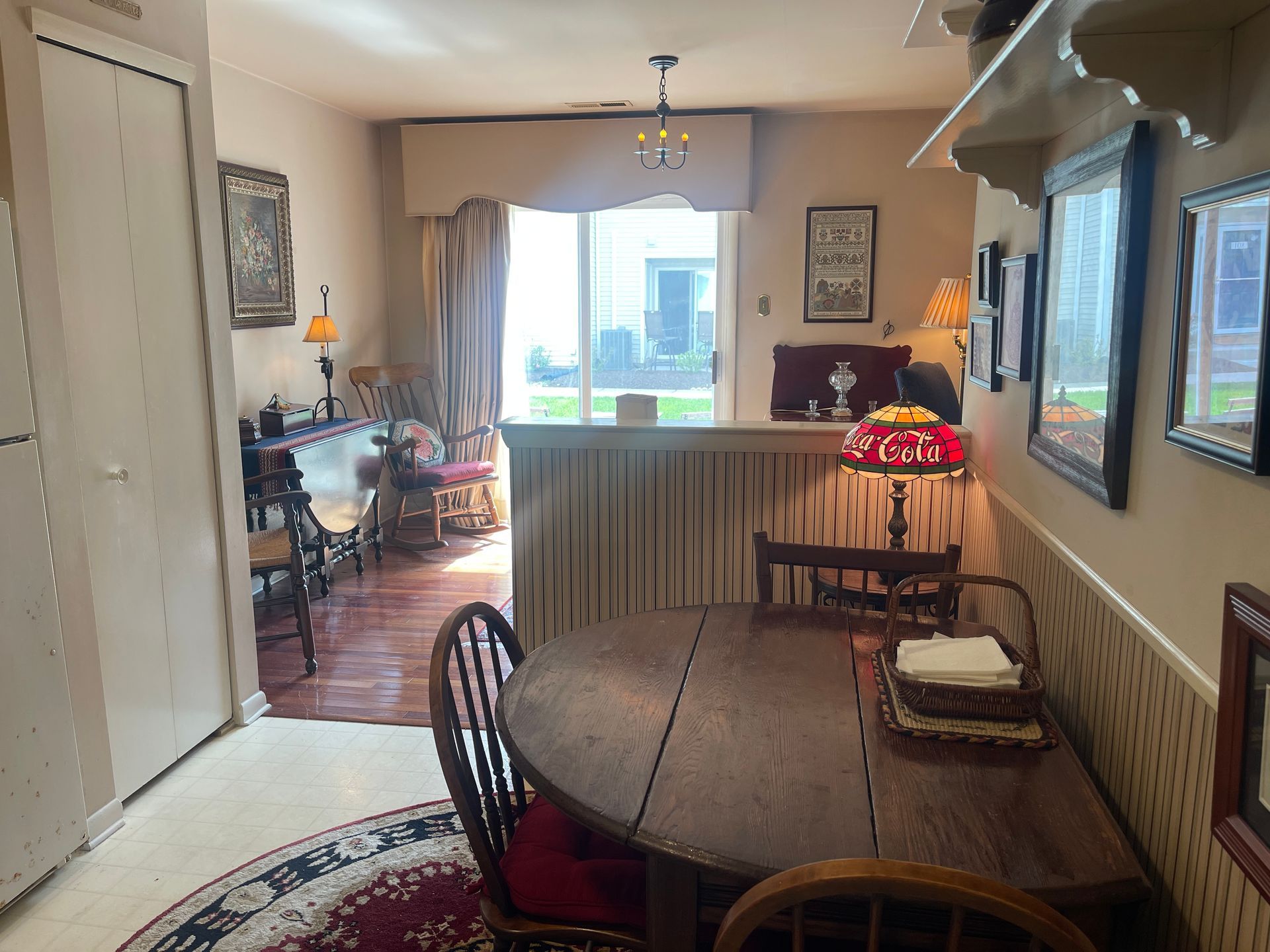 A cozy dining room and living space with a round table, lamp, rug, and bright windows.