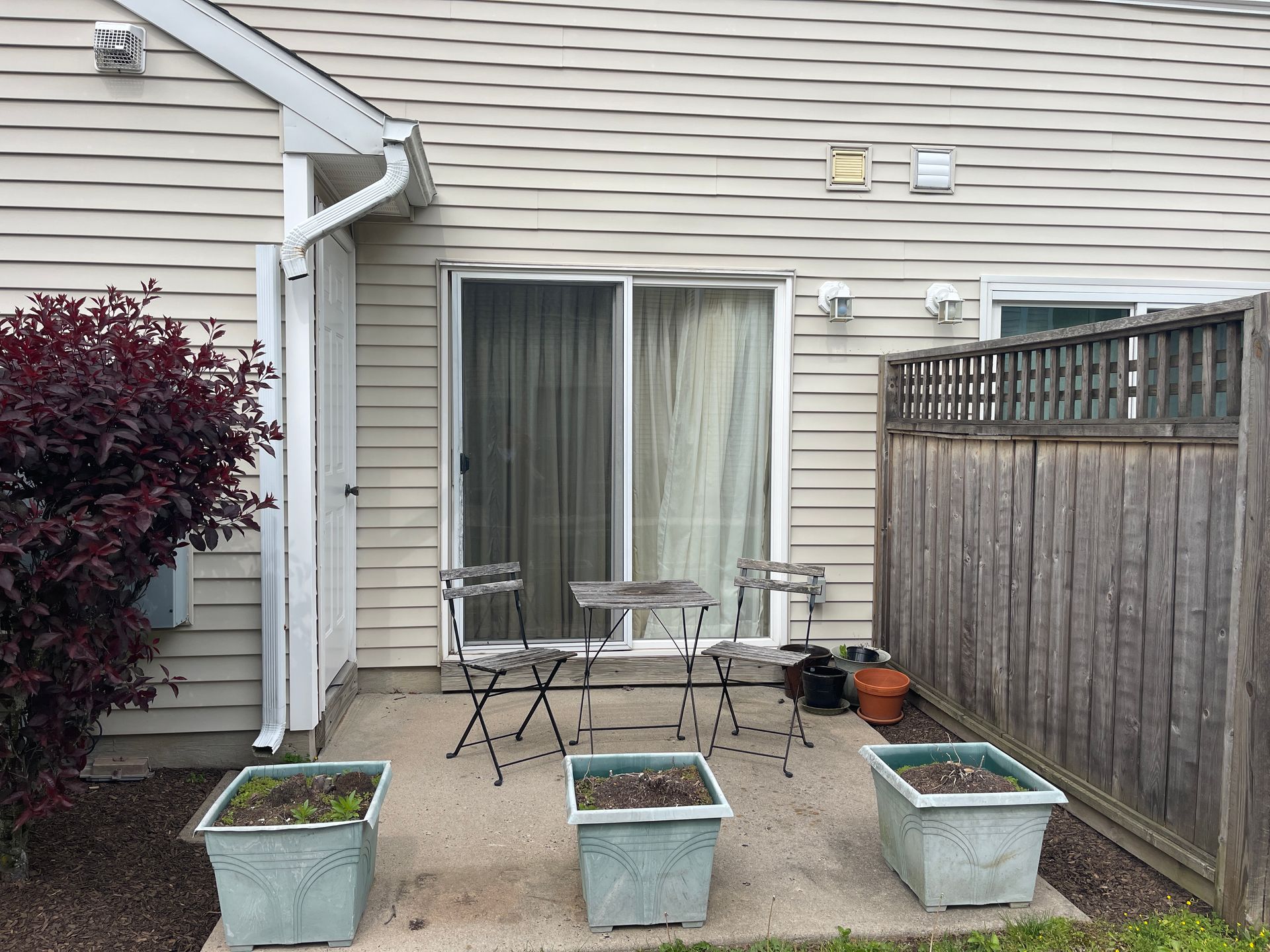 Back patio with sliding door, patio table and chairs, three planters, and a wooden fence on the right.