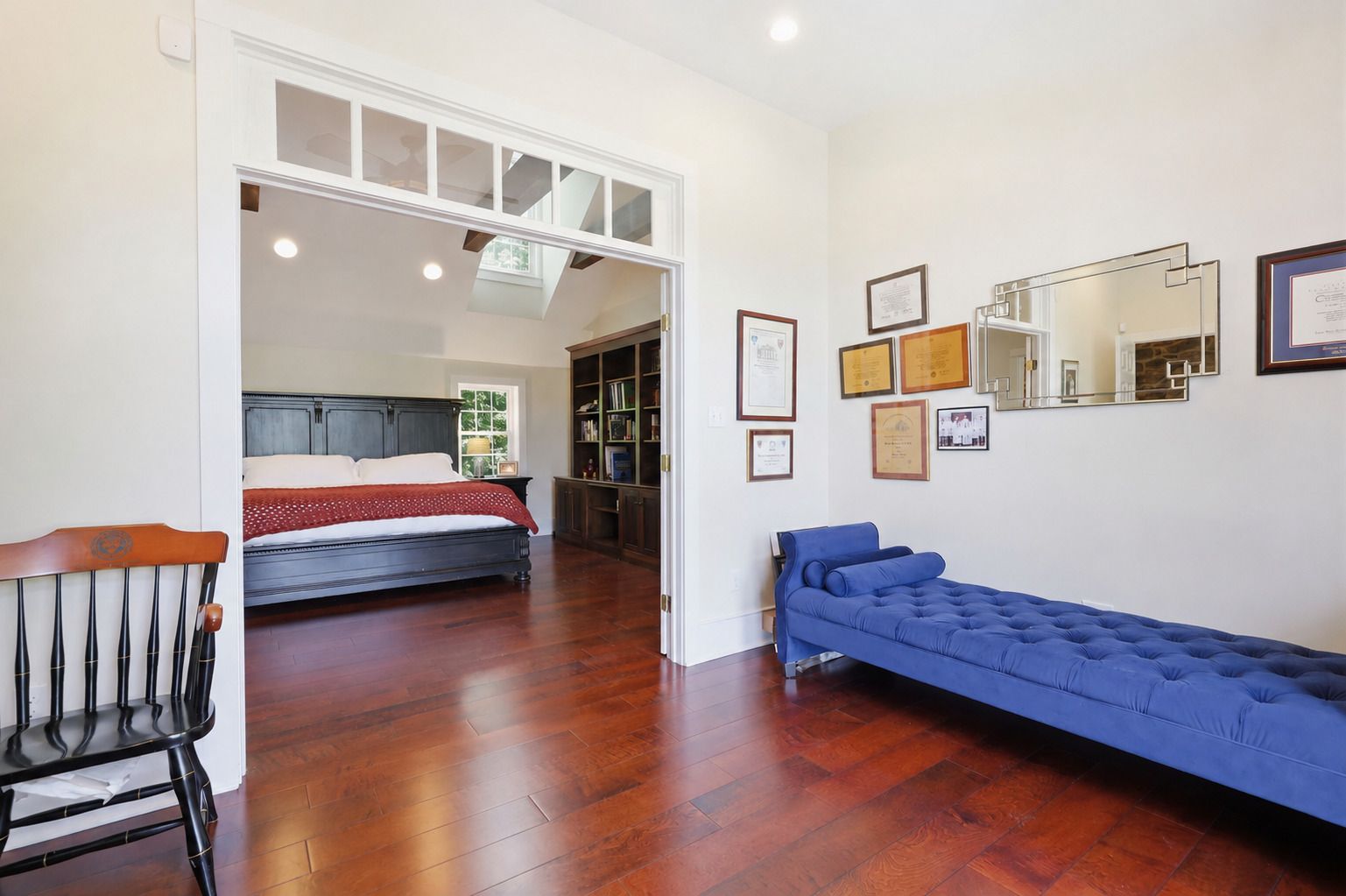 Bright bedroom with hardwood floors, blue daybed, wall art, and a bed visible through the doorway