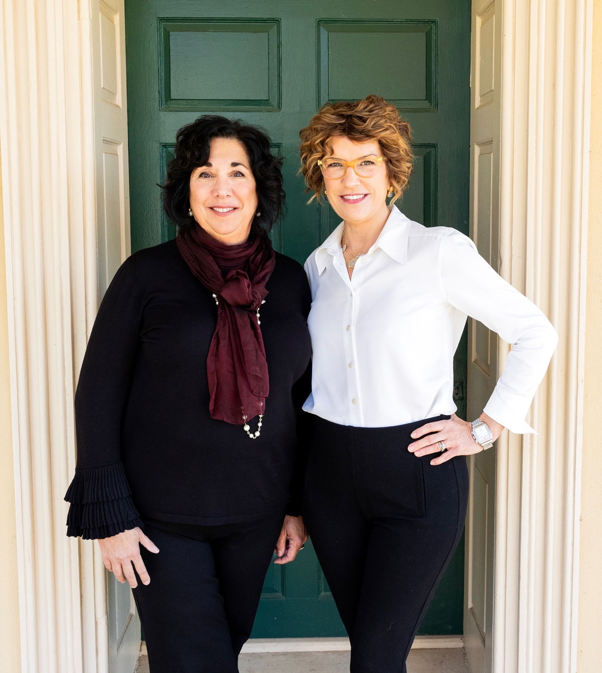 Two women standing in front of a green door; one wearing black, the other white.