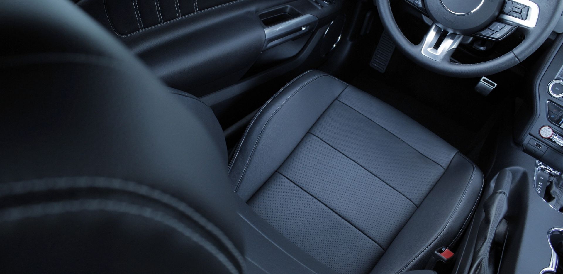 Interno di un'auto nera con sedili in pelle. Volante visibile sullo sfondo.