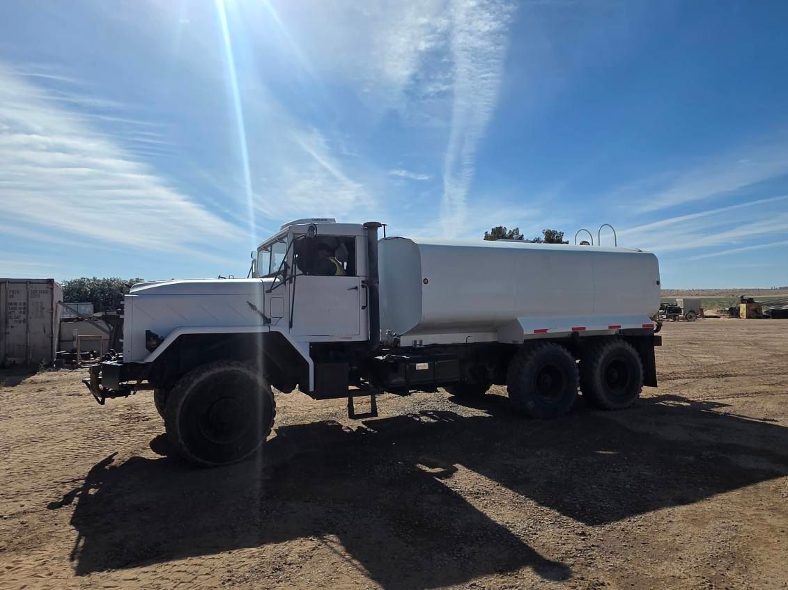 White dump truck parked on a dirt lot under a bright blue sky