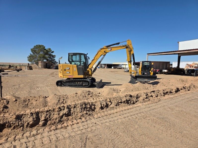 Yellow excavator working on a dusty construction site near a building under a clear blue sky