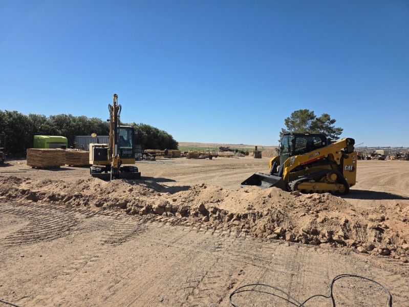 Two excavators working on a sandy construction site under a clear blue sky