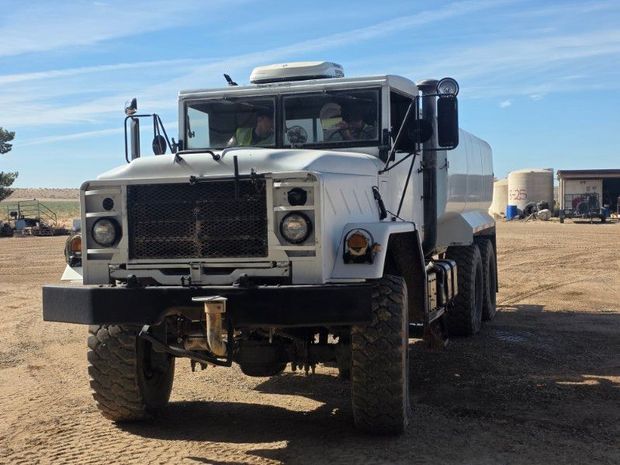 White dump truck parked on a dirt lot under a bright blue sky