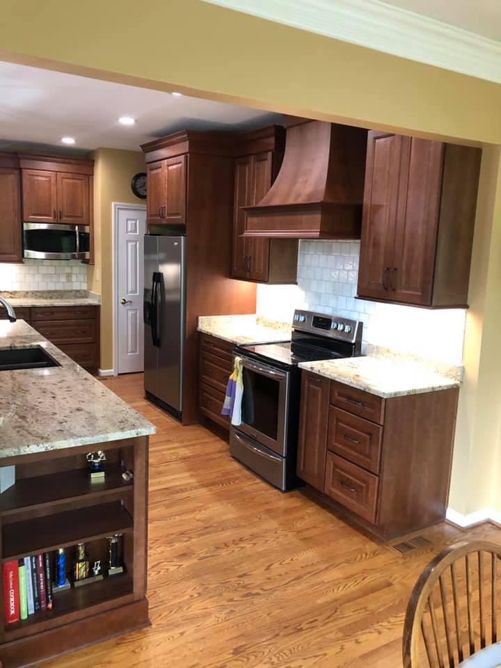 A kitchen with wooden cabinets, stainless steel appliances, and a granite countertop; yellow walls and hardwood floors.