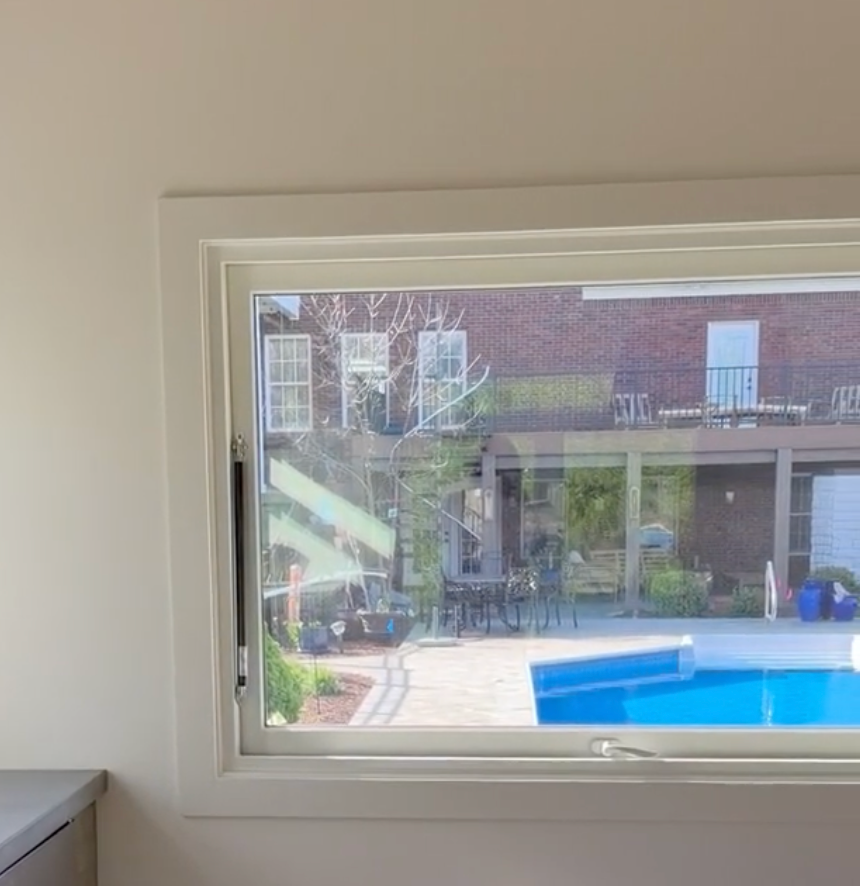 View through a window of a courtyard with a blue swimming pool and brick building beyond