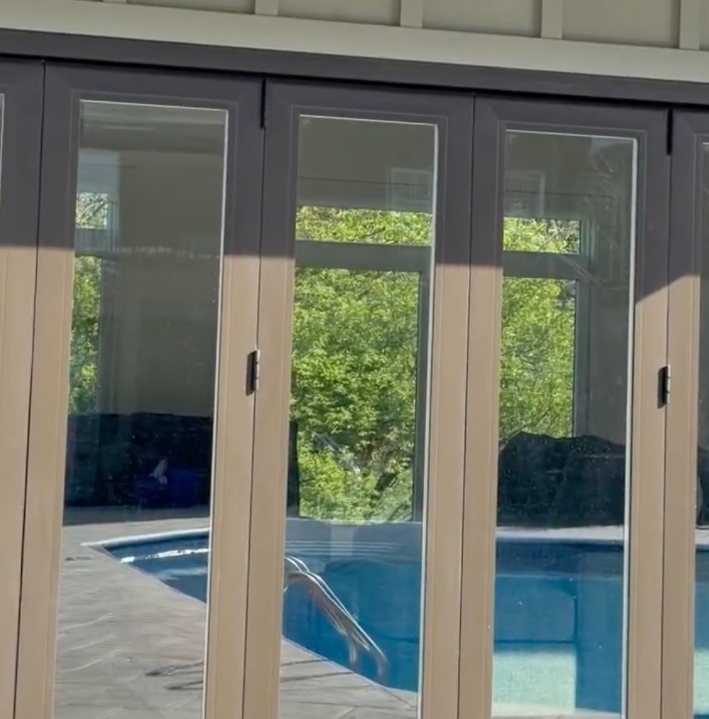 Sliding glass doors opening to a patio and blue swimming pool, with green trees outside