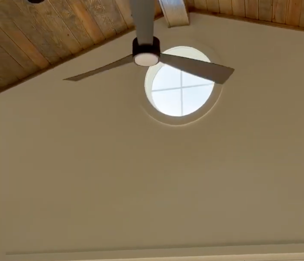 Ceiling fan and round window on a beige wall with a wood-paneled ceiling