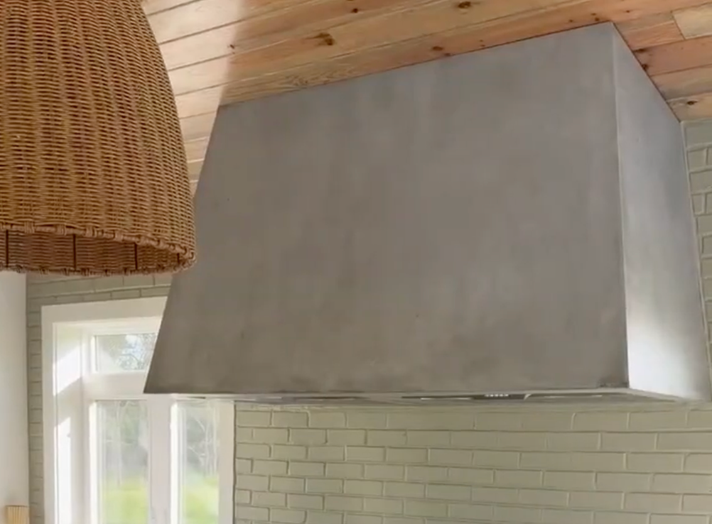 Large gray kitchen range hood above a white tiled backsplash in a wood-paneled room