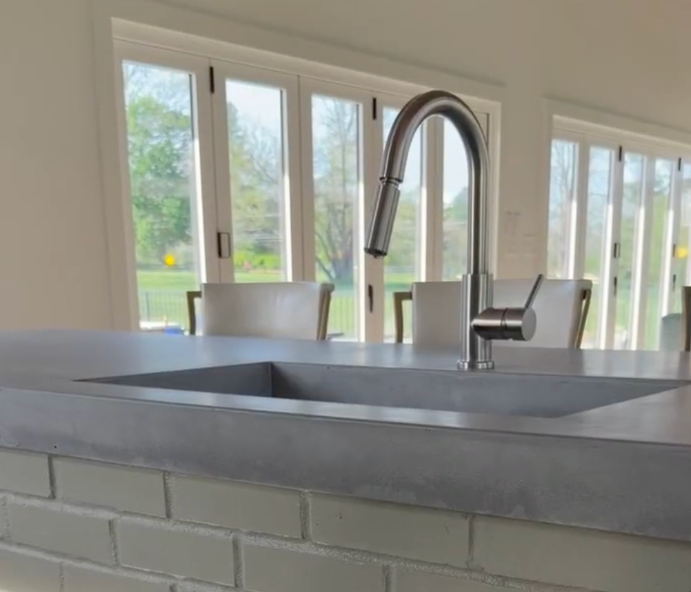 Modern kitchen with a gray sink and chrome faucet in front of large windows and a green outdoor view