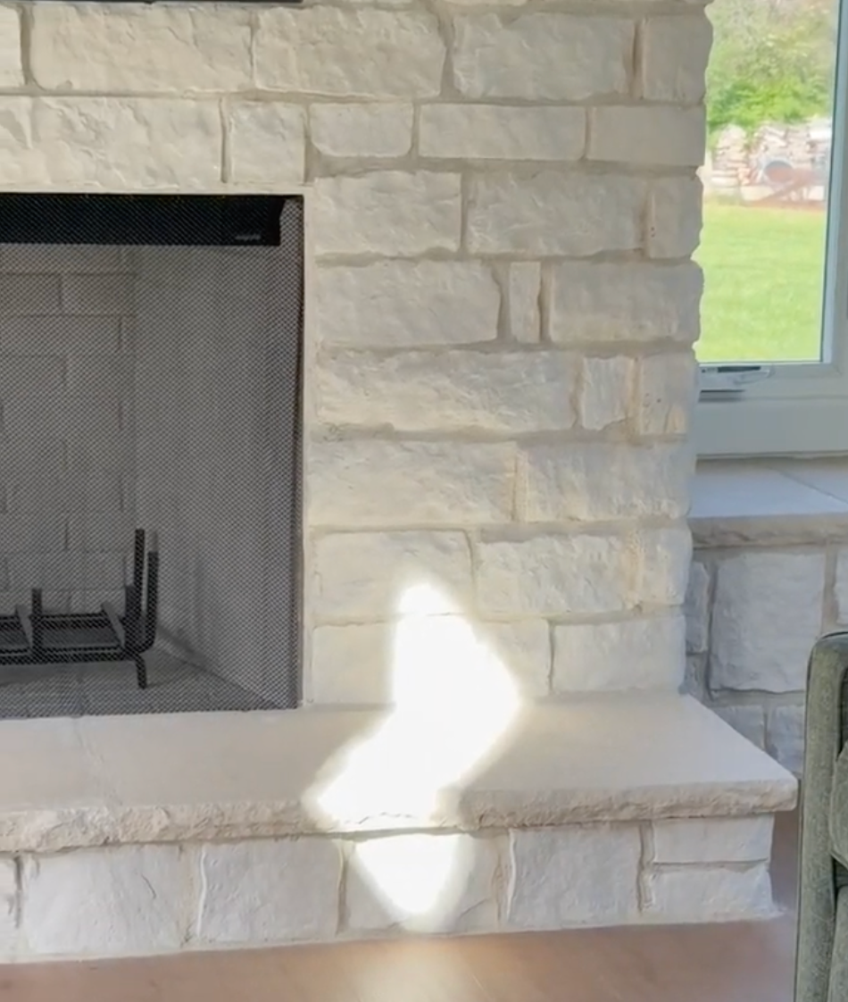 Stone fireplace with black firebox and a bright sunlit patch on the hearth beside a window