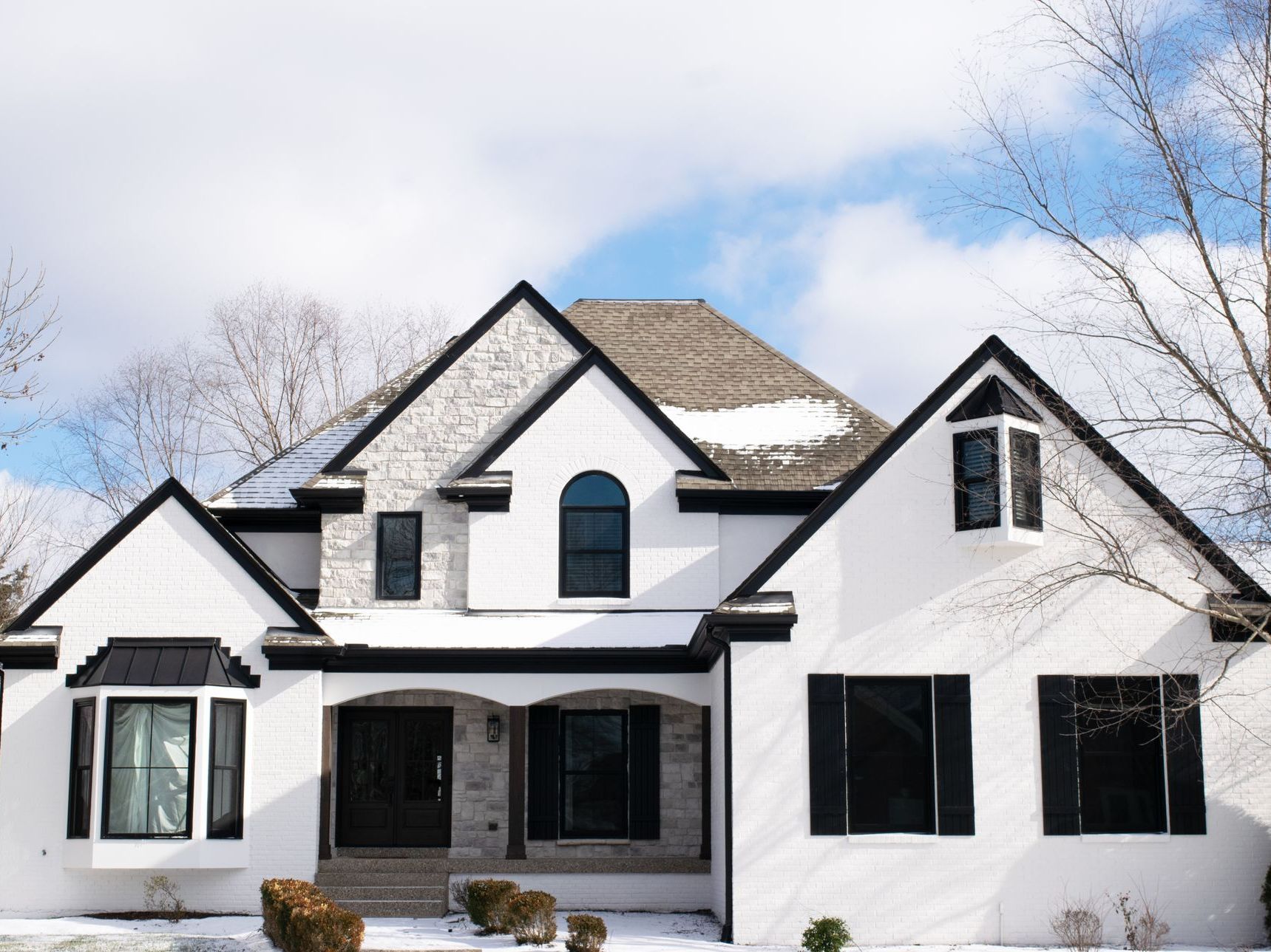 White house with black trim, dark windows, and snow on the roof.