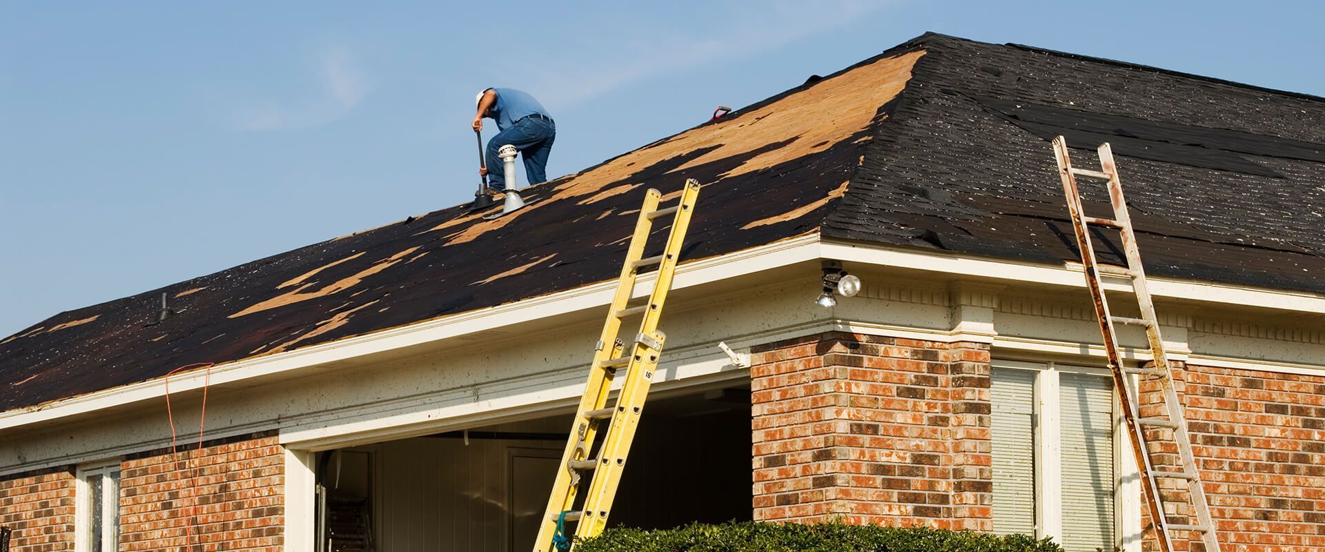 A man is working on the roof of a house with a ladder.