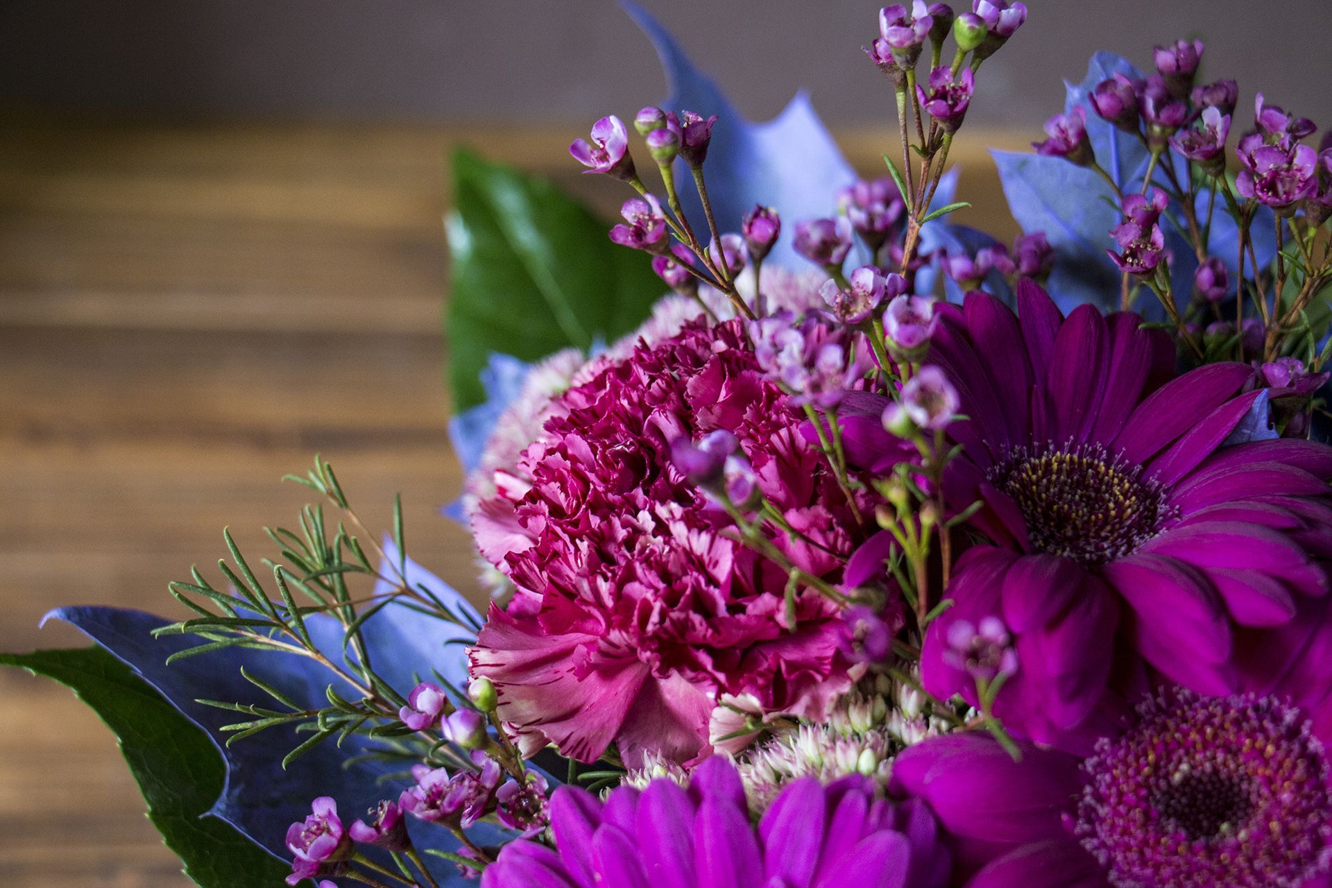 Purple and pink flowers with green leaves in a bouquet against a blurred brown background