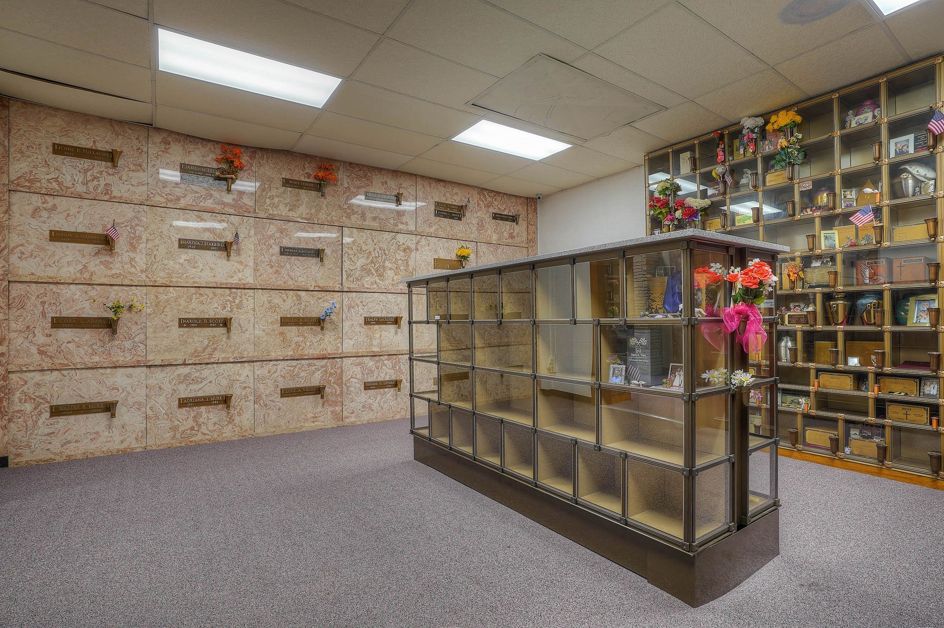 Spacious memorial room with wall niches, glass display cases, and overhead fluorescent lights.