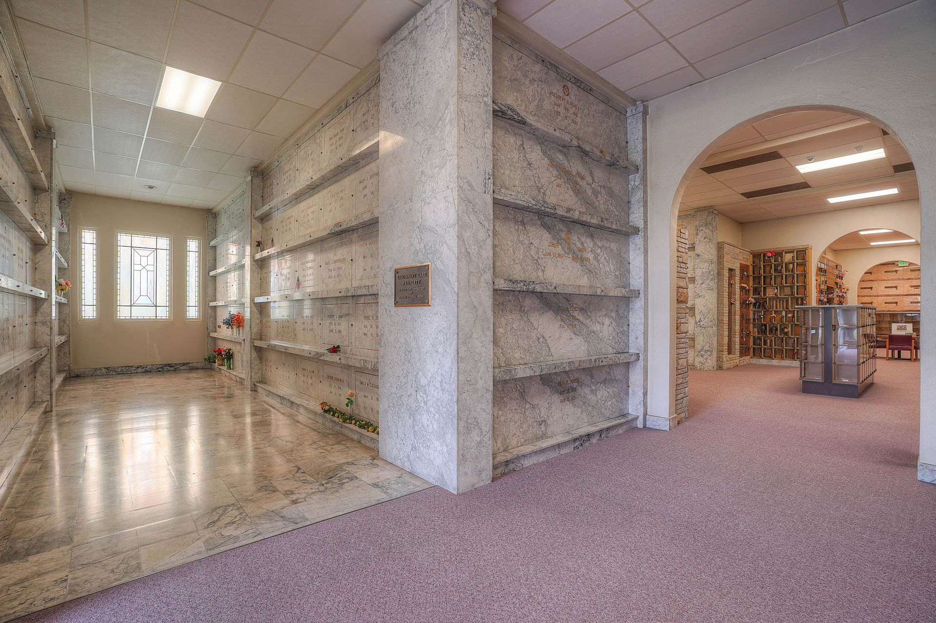 Empty office lobby with carpet, tiled hallway, shelving, and an archway into another room.