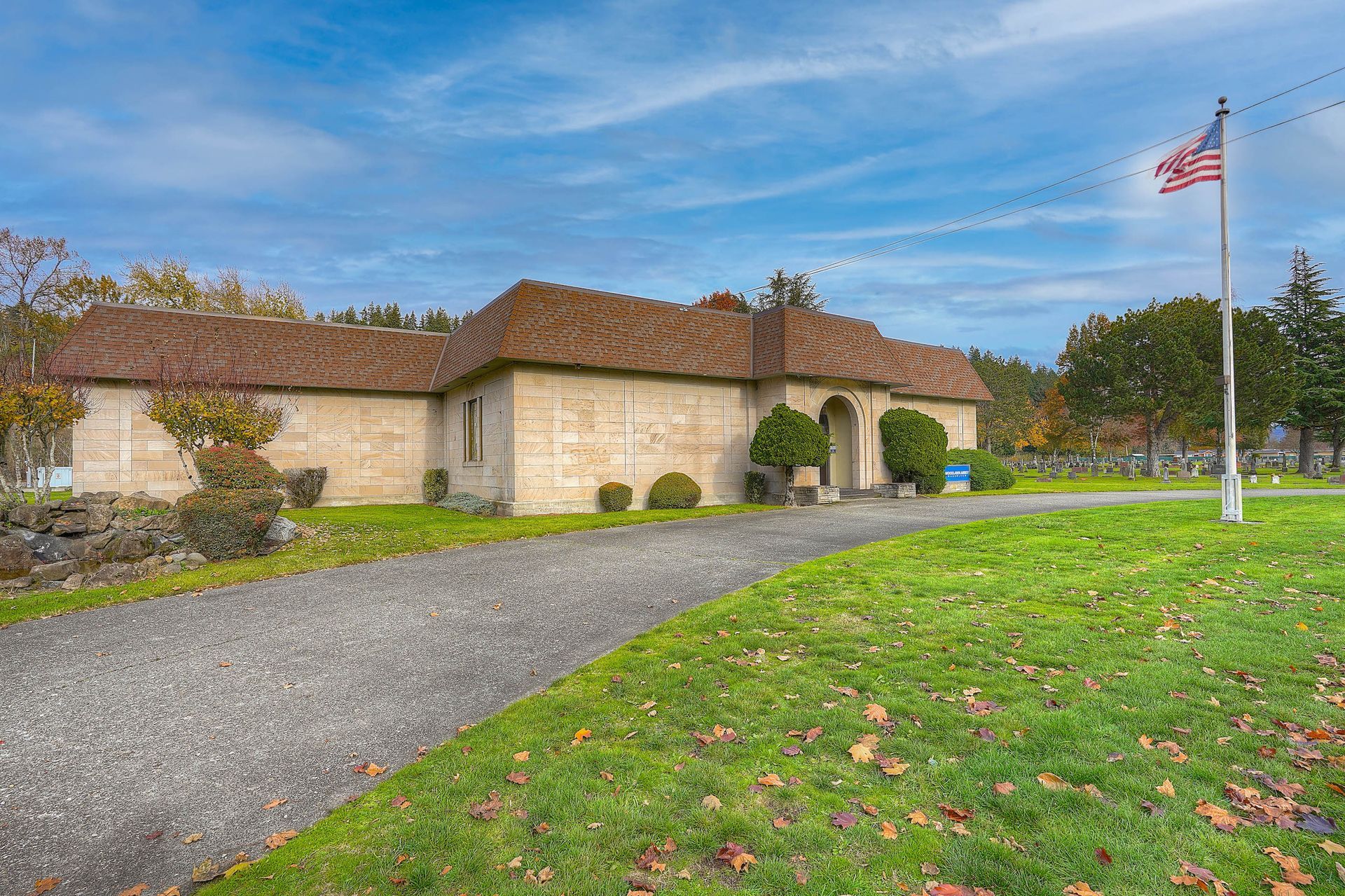 Single-story stone house with a red-tile roof, gravel driveway, and an American flag in the front yard.