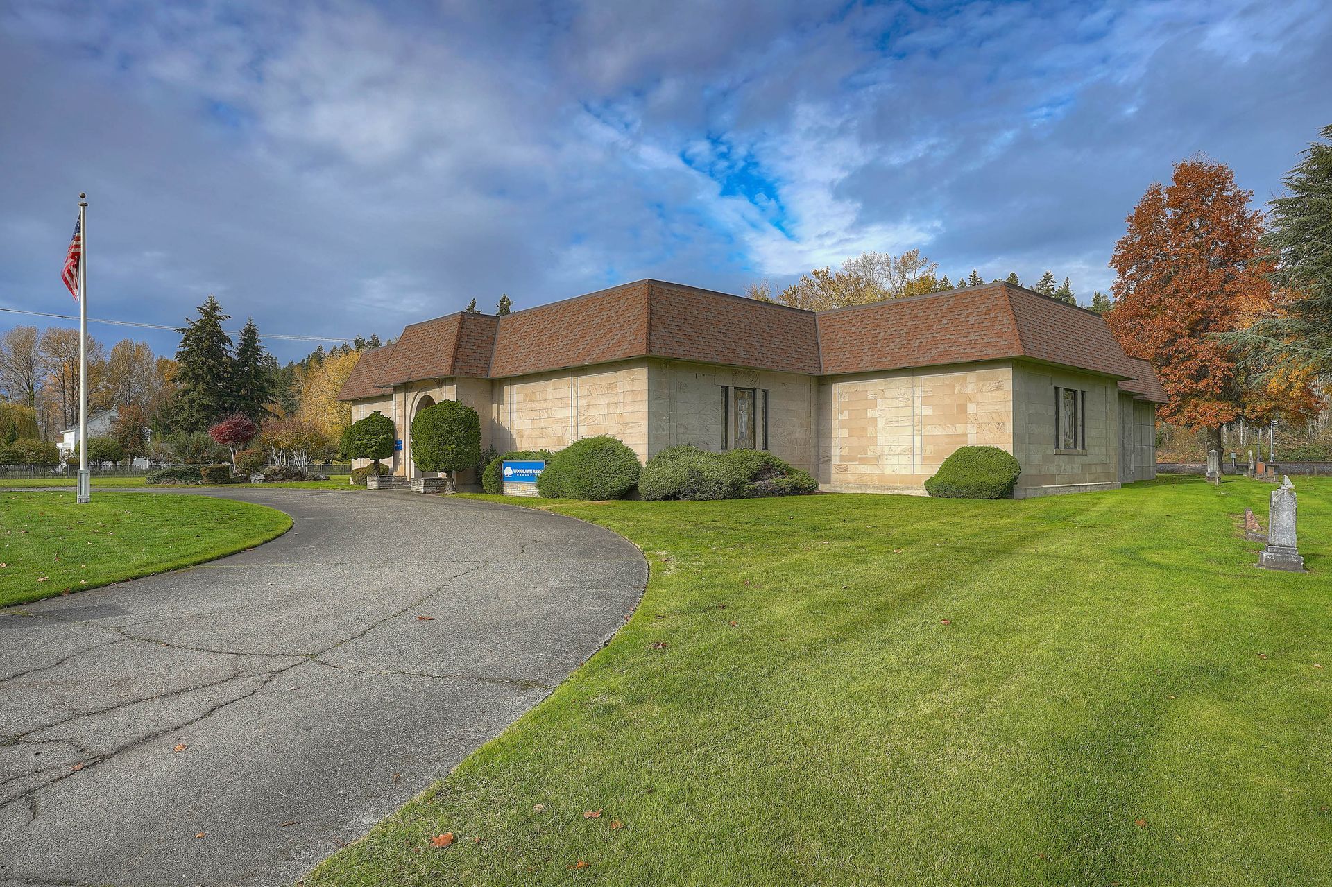 Single-story brick building with brown roof beside a curved driveway and grassy lawn under a blue sky