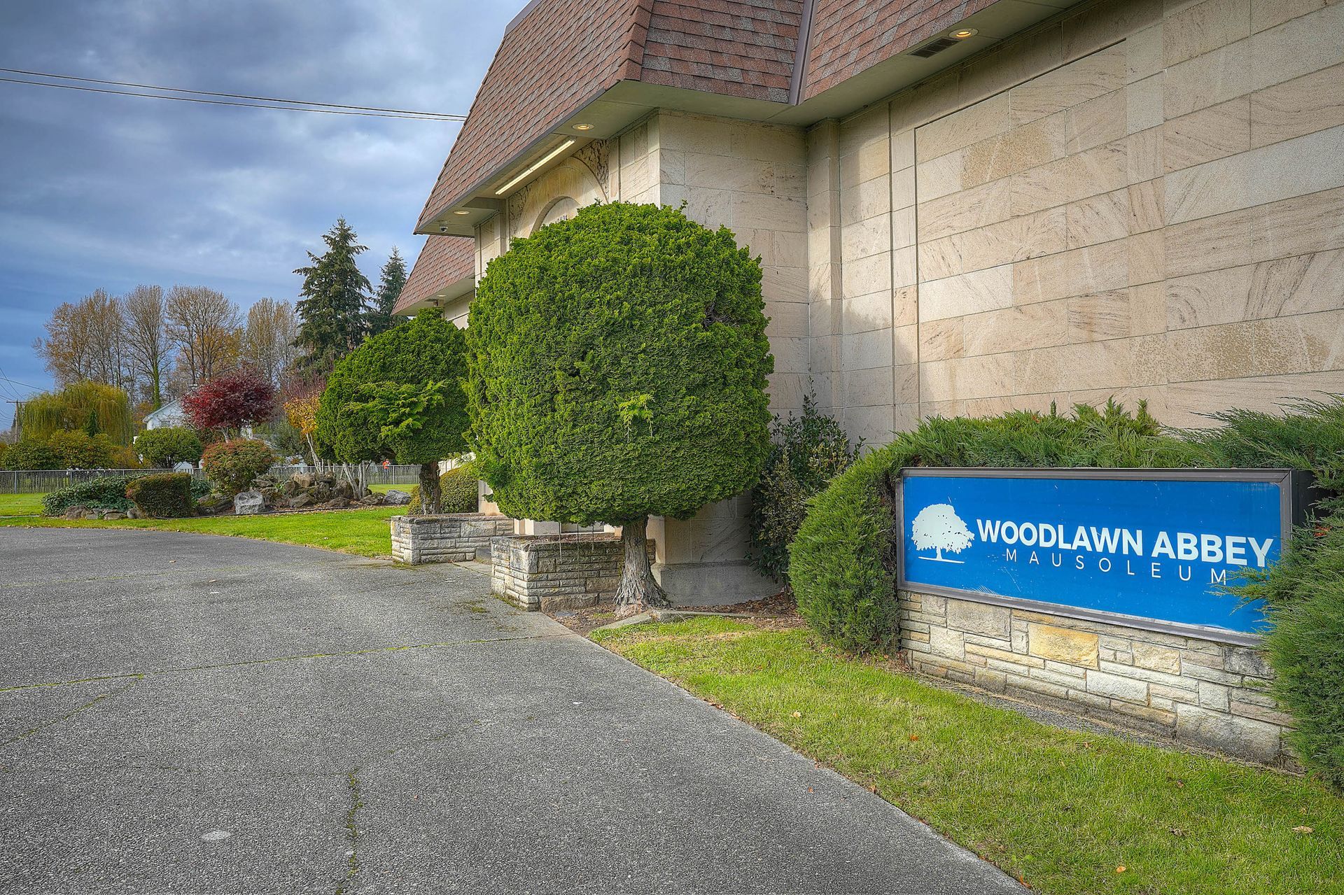 Woodclan Abbey sign beside gravel path and trimmed hedges outside a stone building