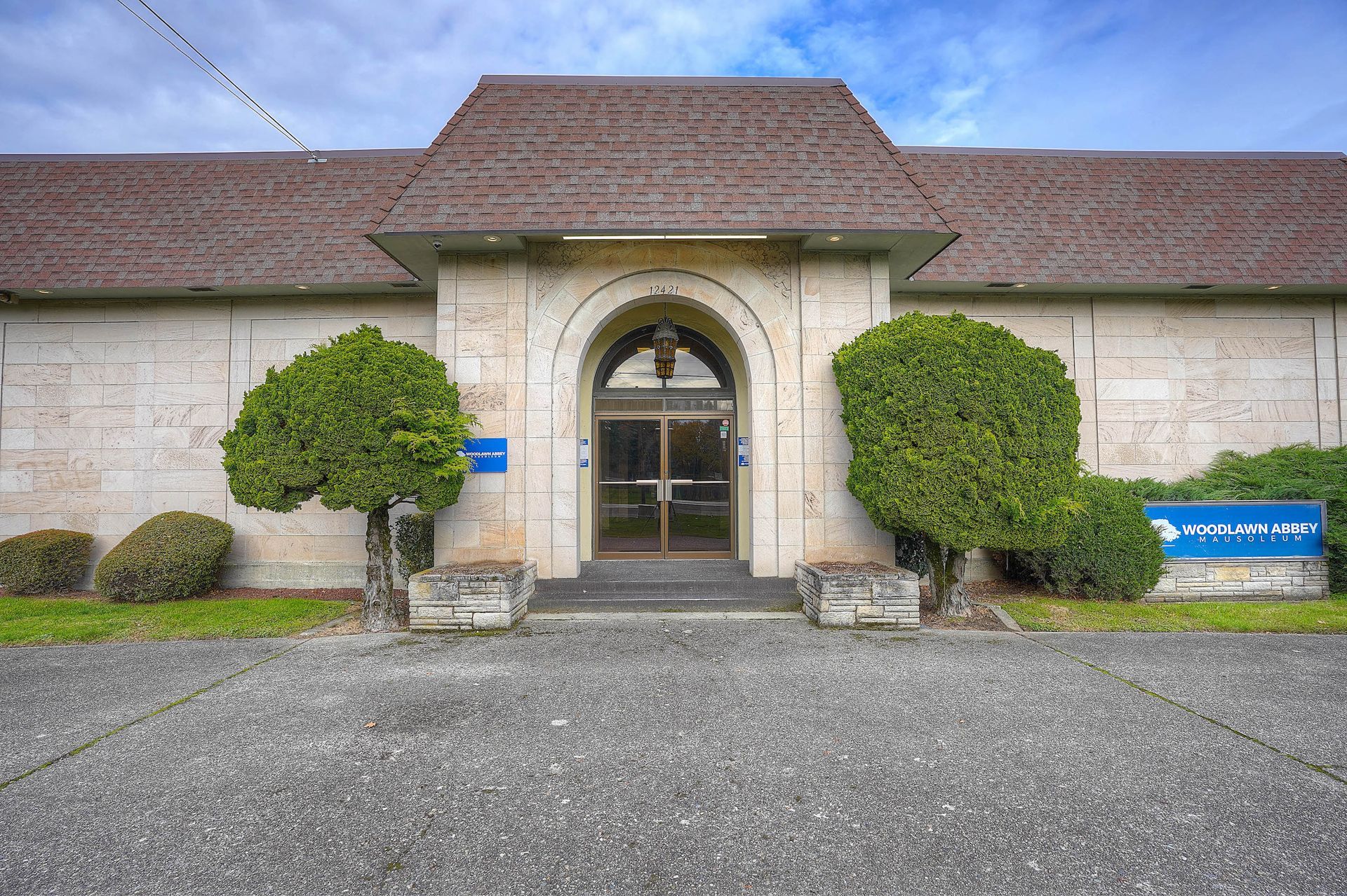 Front entrance of a stone building with an arched doorway, trimmed bushes, and gravel driveway.