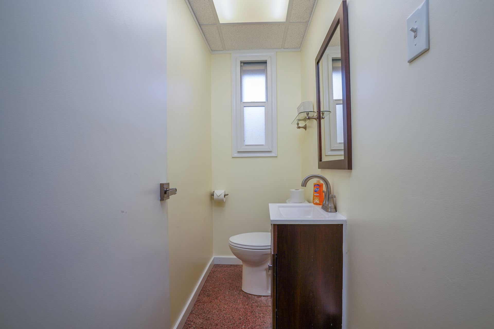 Small bathroom with a toilet, sink, mirror, and narrow window.