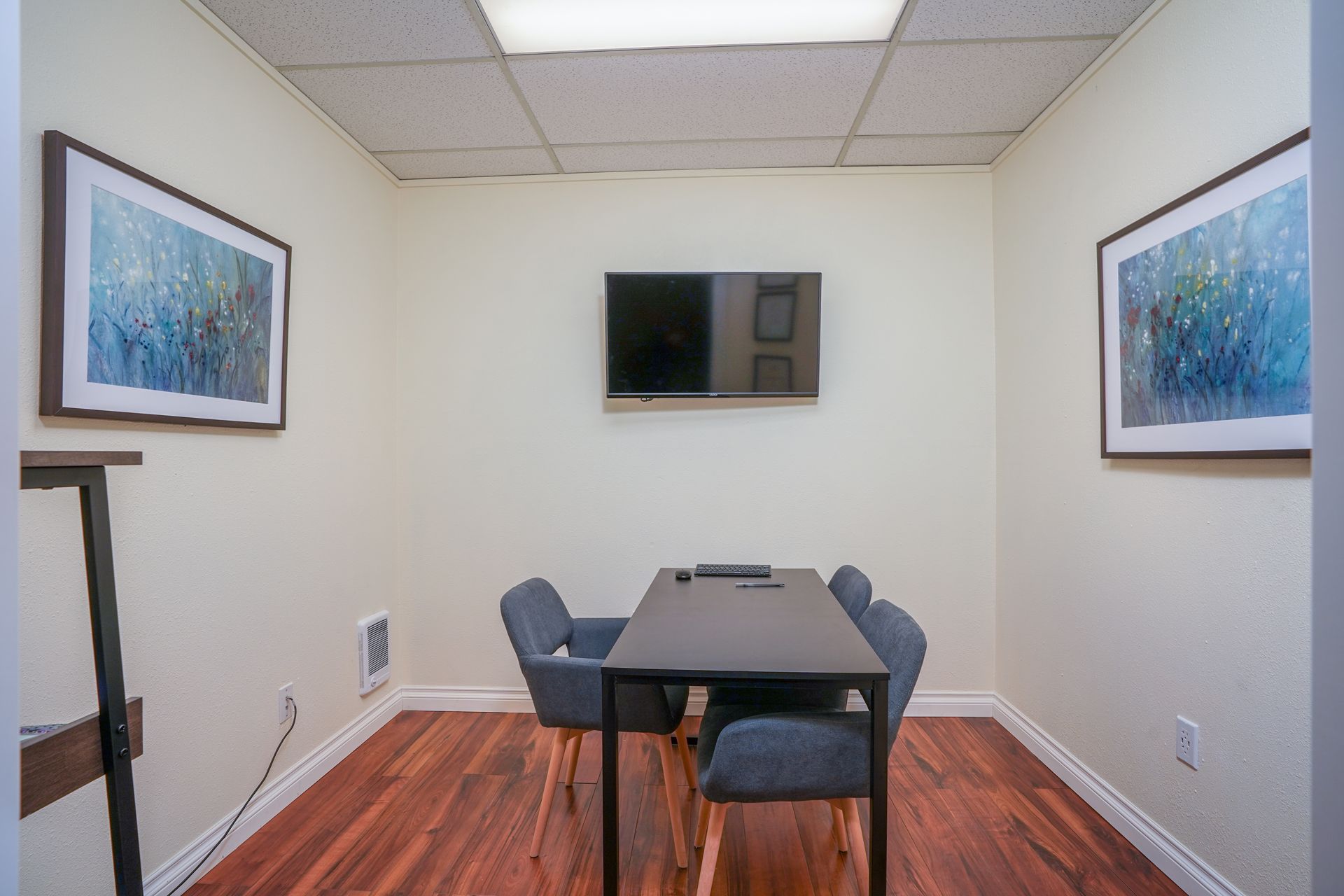 Small conference room with a table, chairs, wall-mounted TV, and framed art on white walls.