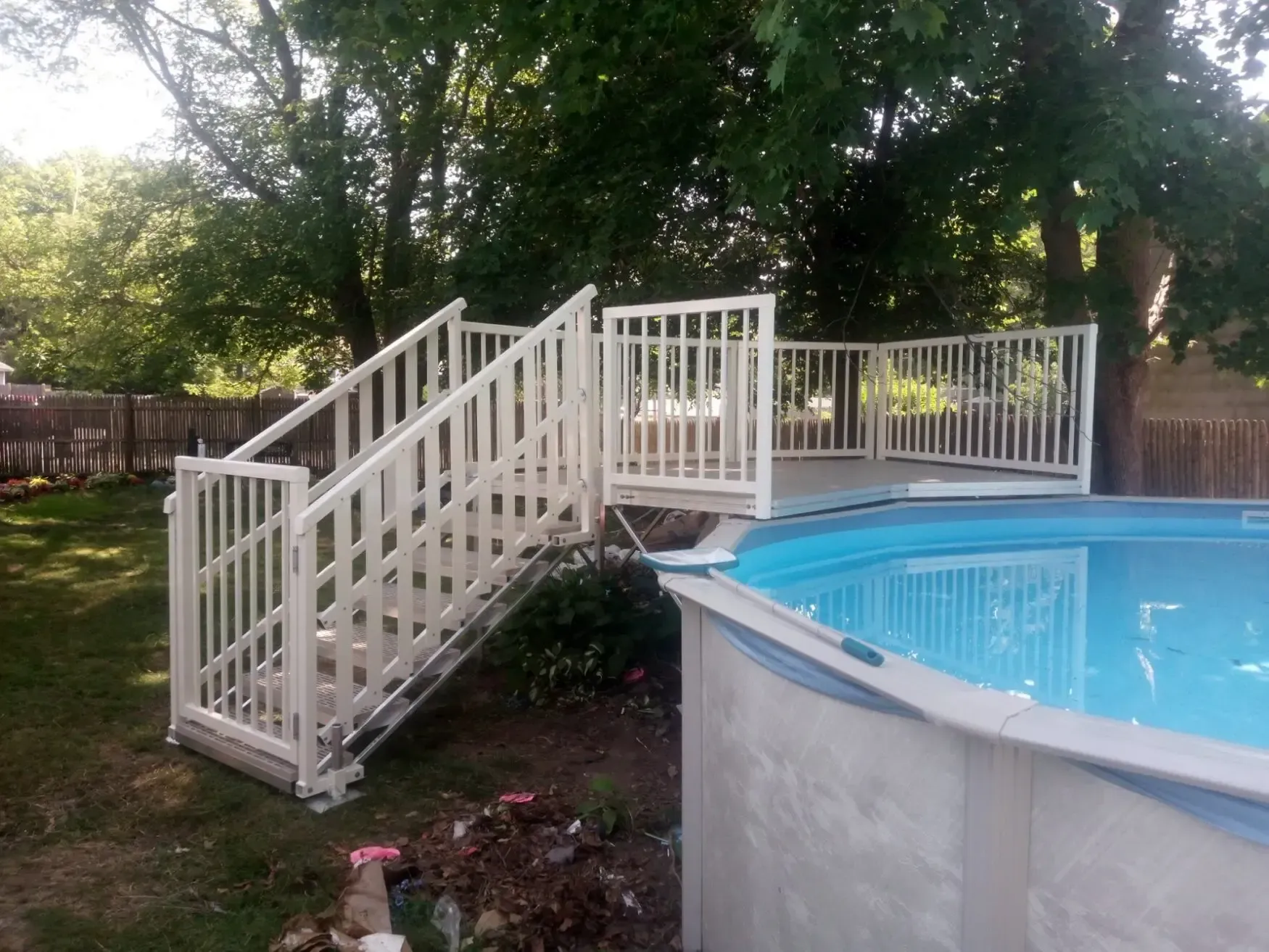 Backyard above-ground pool with white stairs and railing, surrounded by trees and a fence