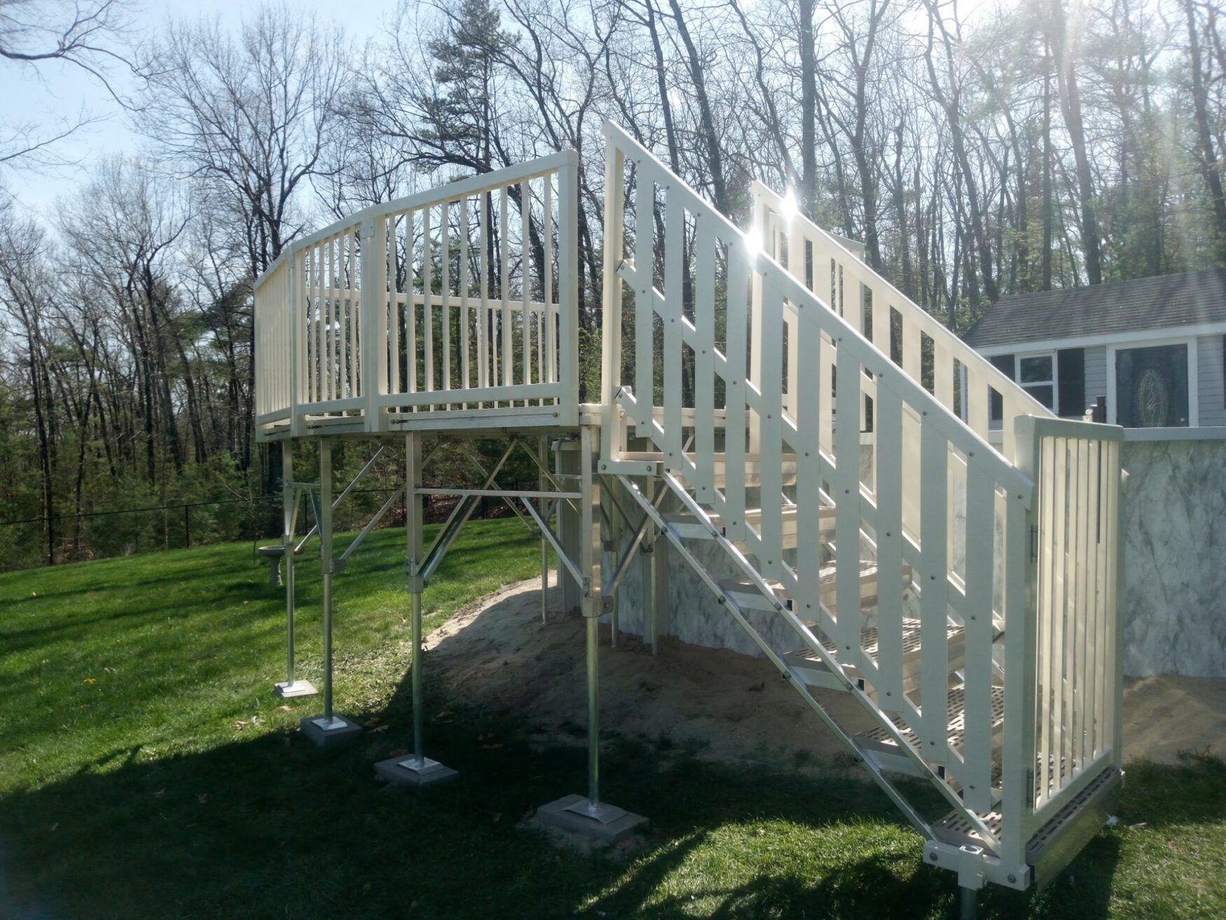 Raised wooden deck stairway with railings on metal supports in a grassy wooded yard