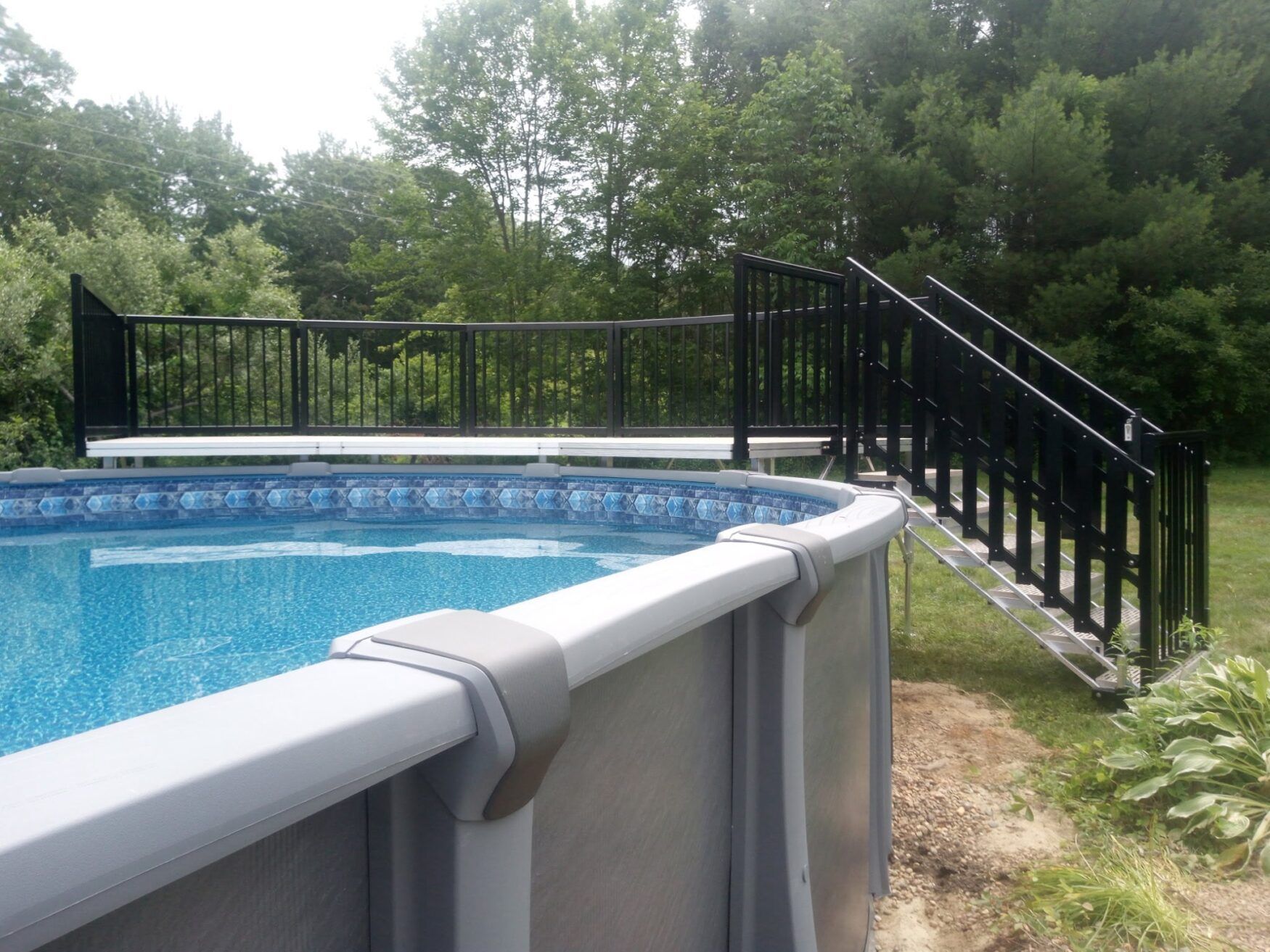 Backyard above-ground pool with black metal fence and stairs, surrounded by trees