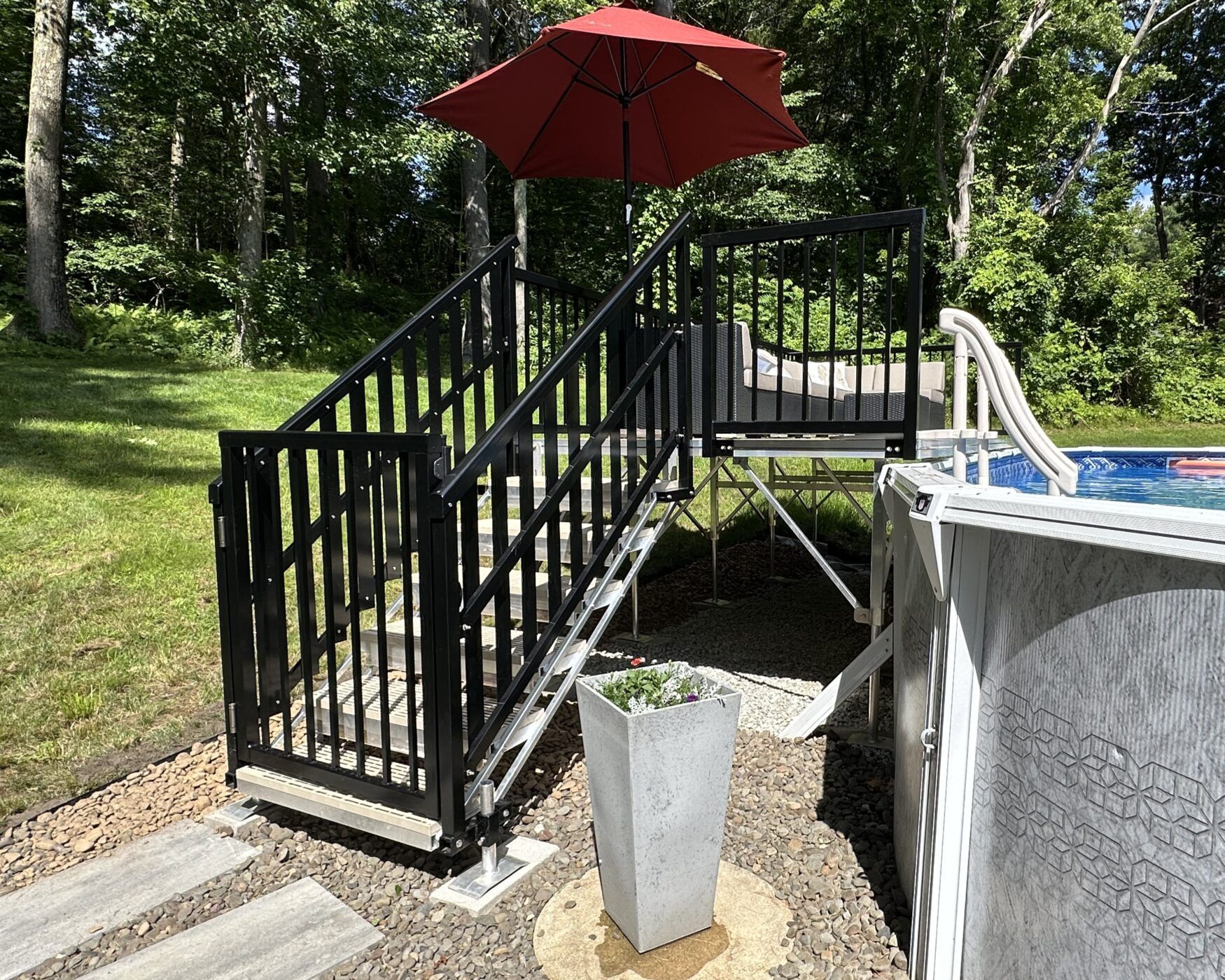 Backyard deck stairs with black railing, red umbrella, and above-ground pool beside a grassy yard