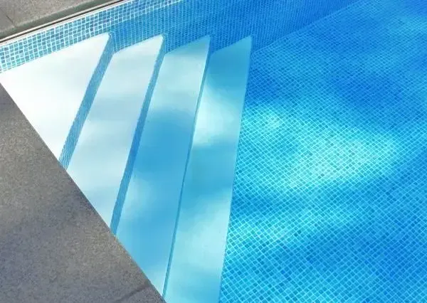 Blue swimming pool with a white diving board and gray deck corner