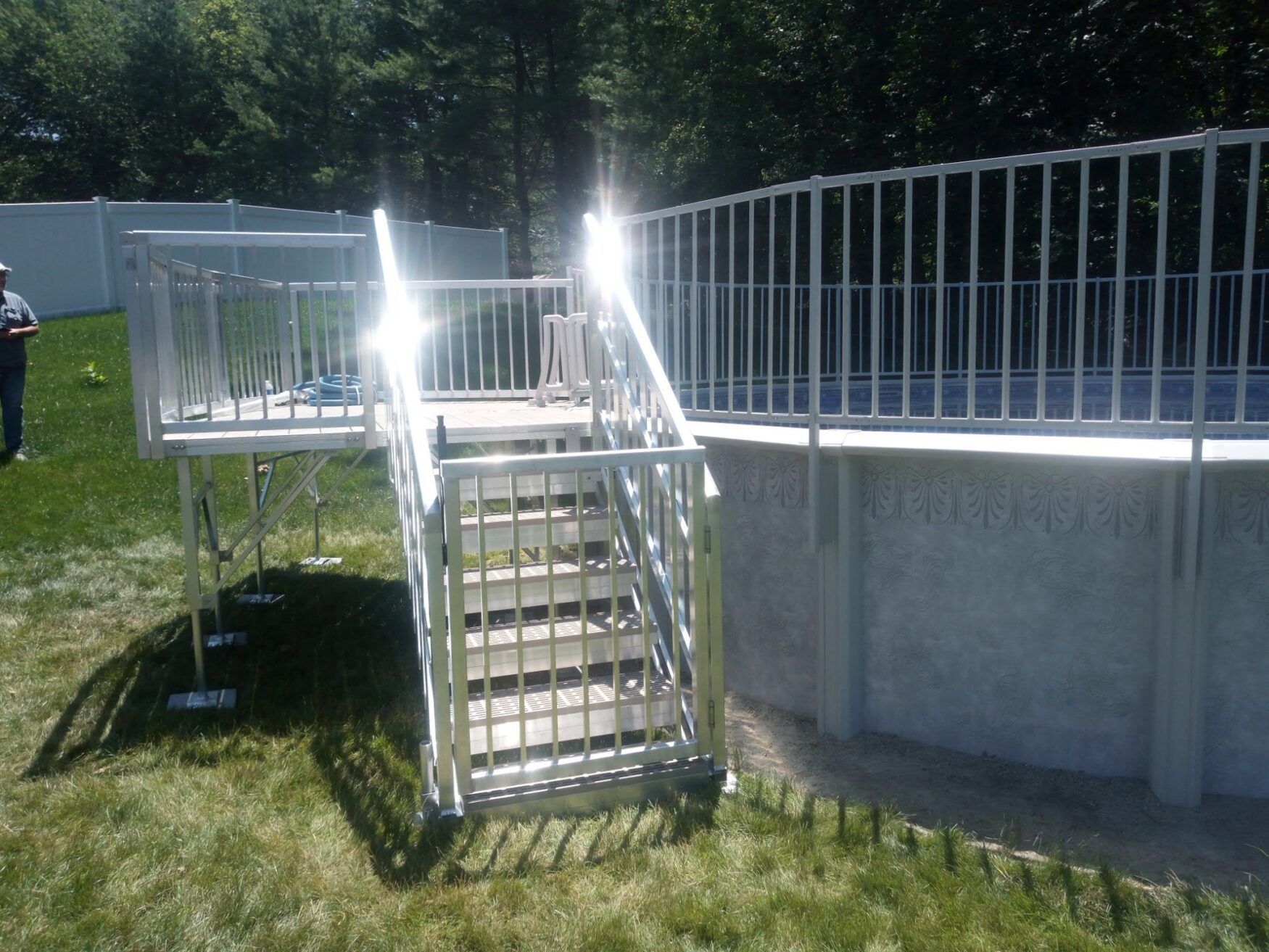 Outdoor metal stairway and ramp beside a raised concrete deck in a grassy wooded area.