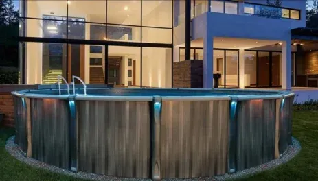 Backyard above-ground pool beside a modern house at dusk