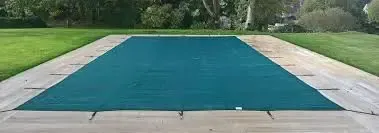 Covered rectangular pool in a landscaped backyard with a blue protective cover